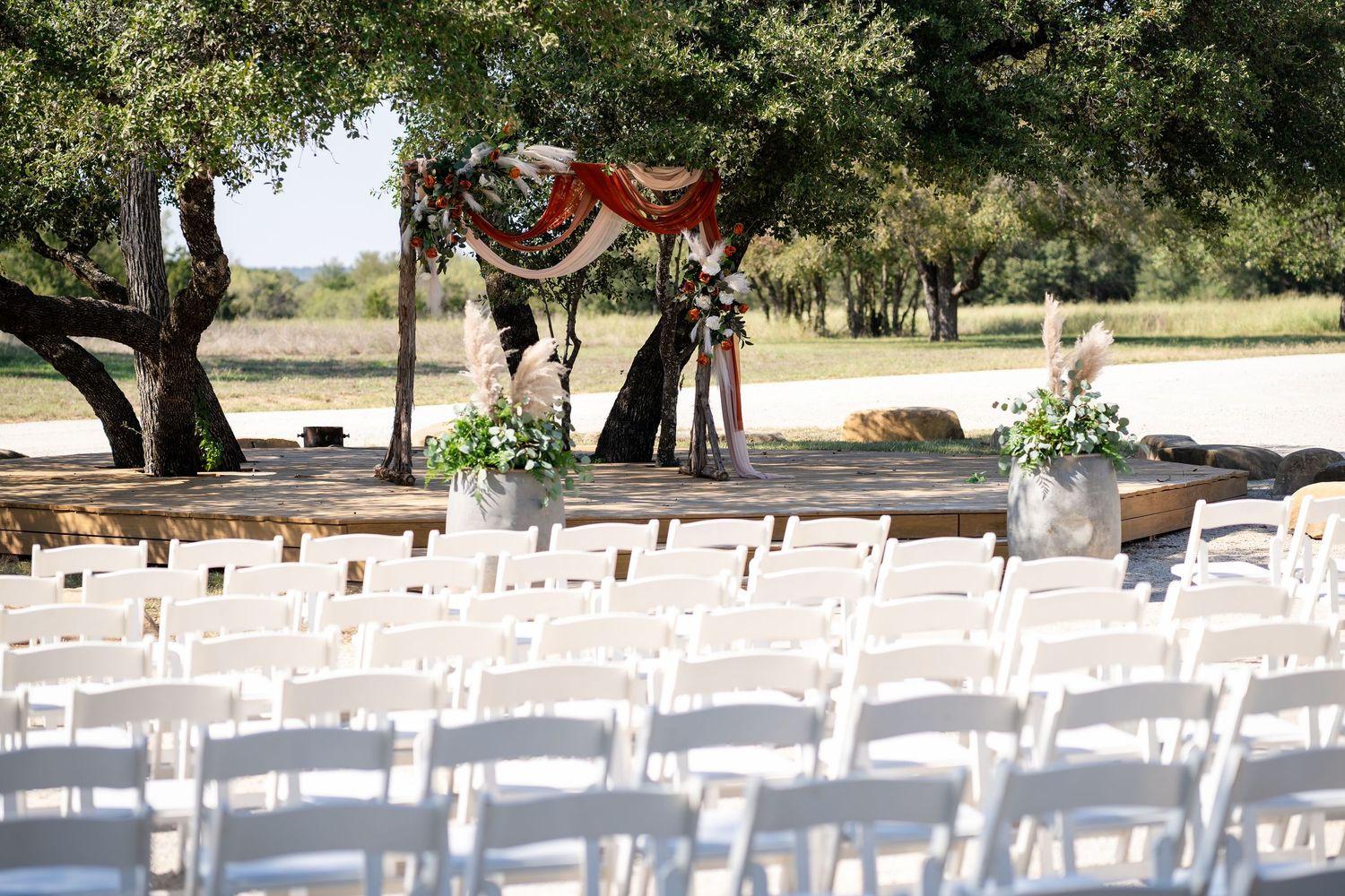 Rows of white chairs set up for outdoor wedding ceremony under trees.