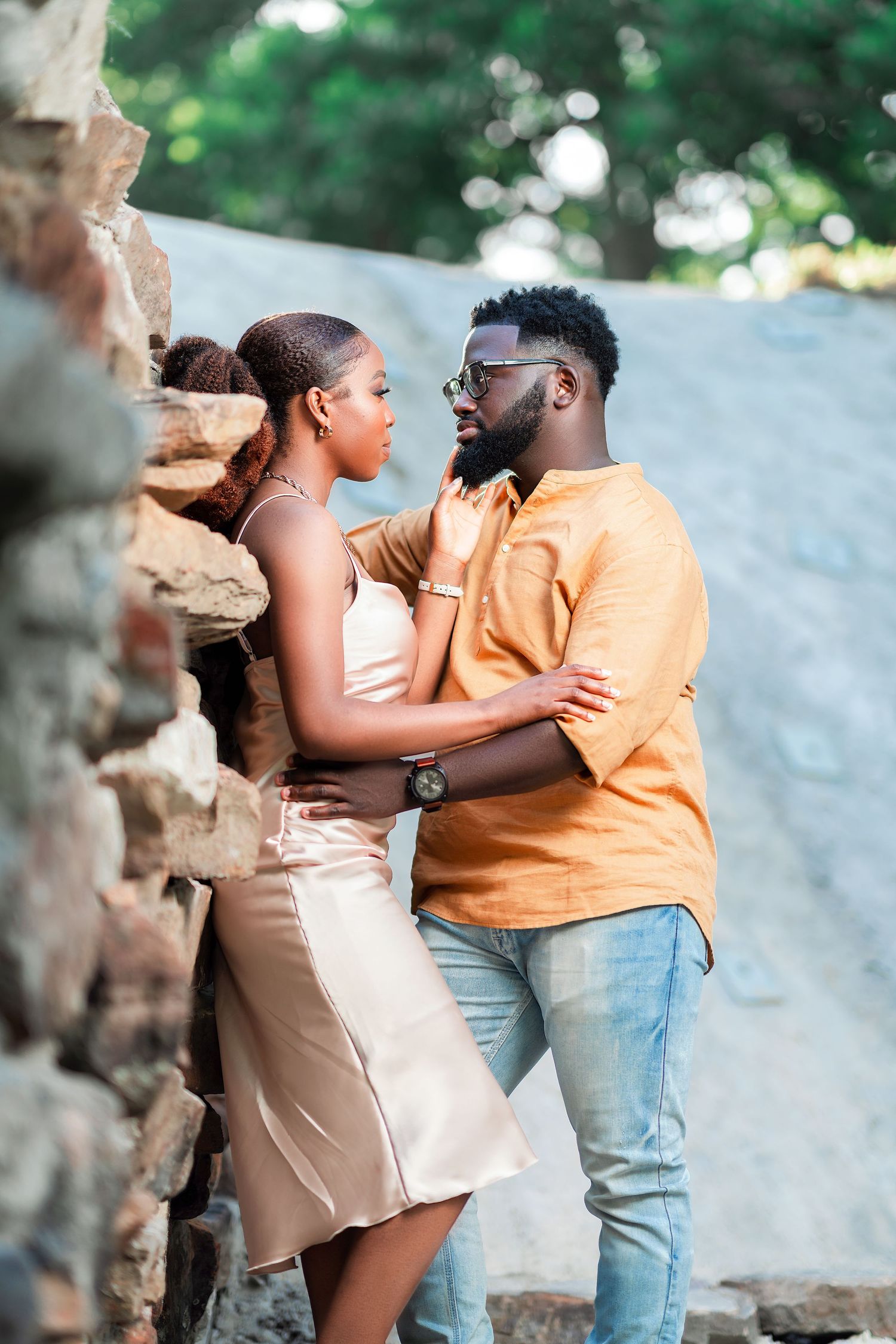 A romantic couple shares a tender moment against a light colored wall outdoors.