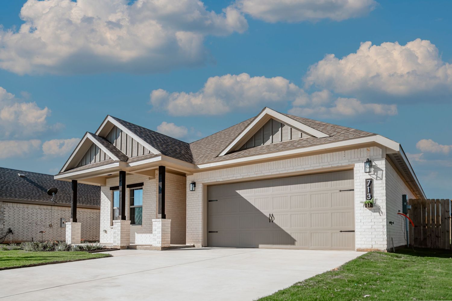 Modern single-story craftsman style home with beige exterior, white trim and attached two-car garage under blue sky.