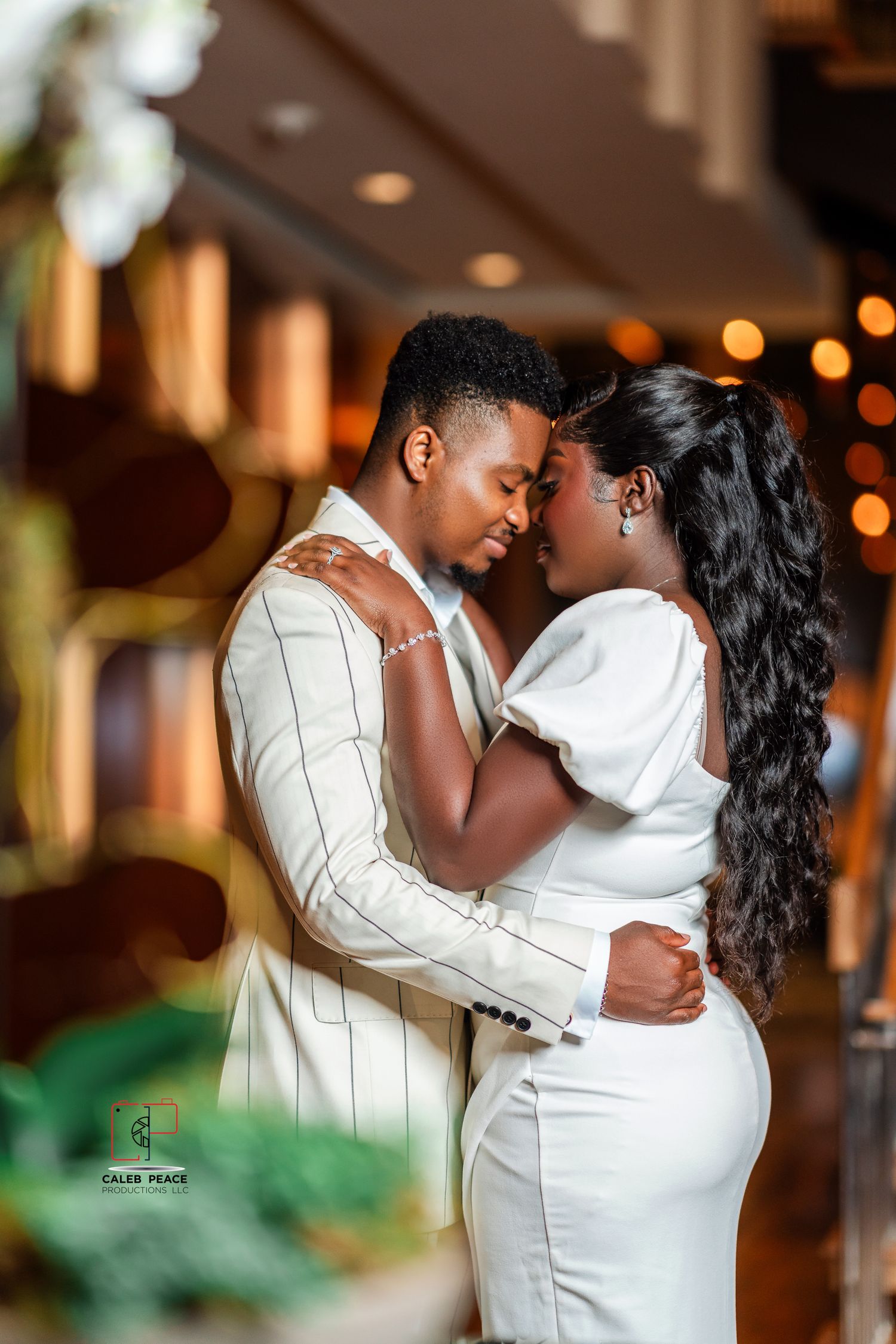 A romantic couple in elegant white outfits share an intimate moment together with soft bokeh lights in the background.
