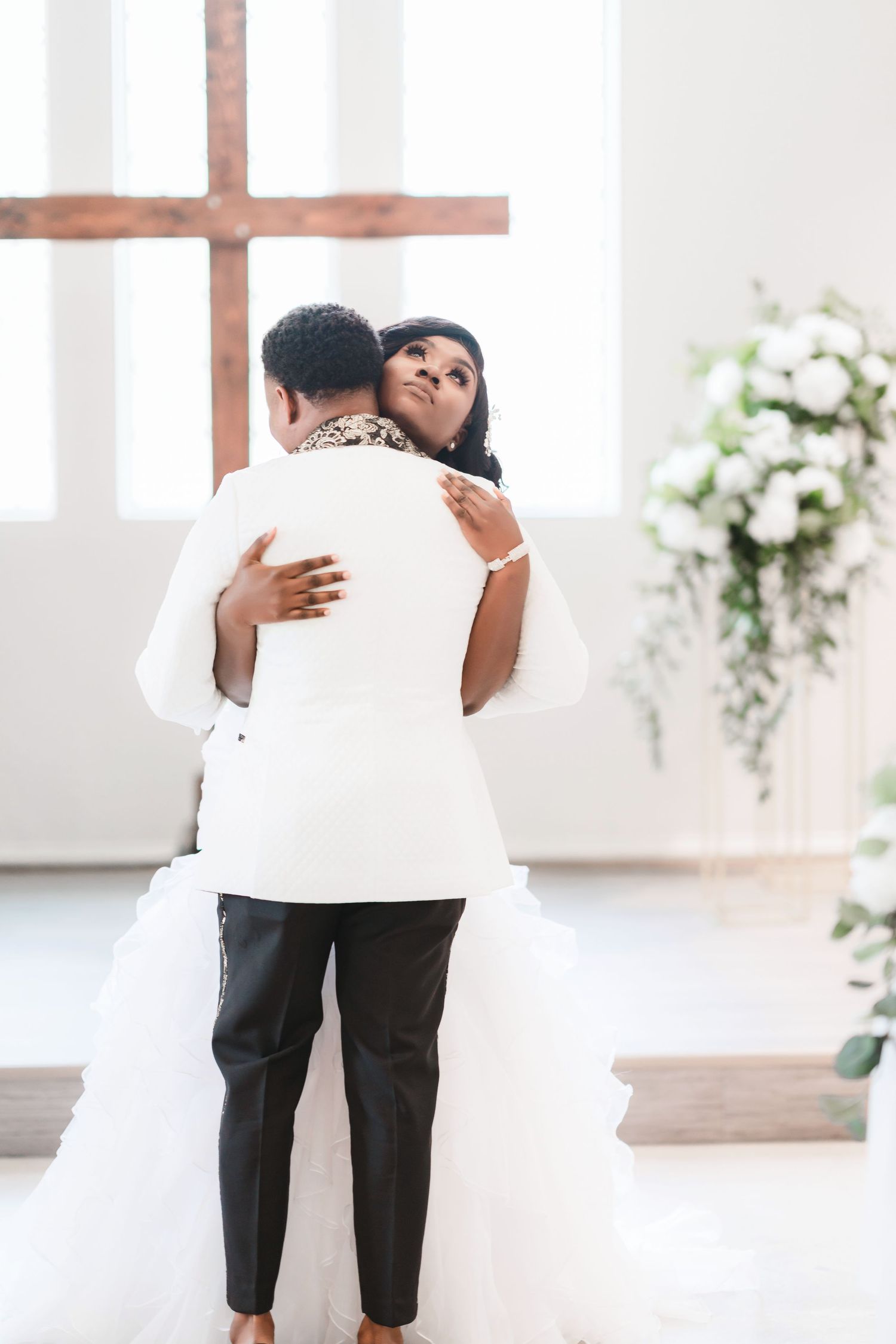 Couple sharing an intimate moment in a bright white chapel with floral decorations.