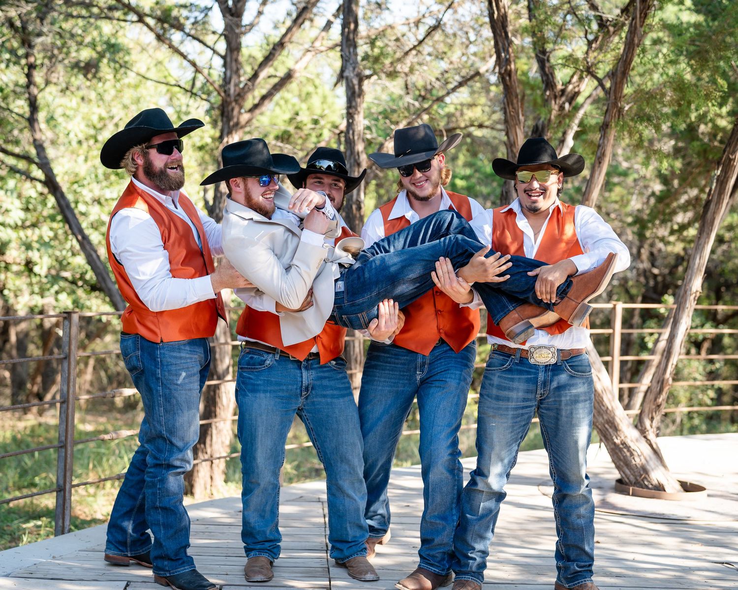Wedding party in western attire strikes playful poses on an outdoor deck.