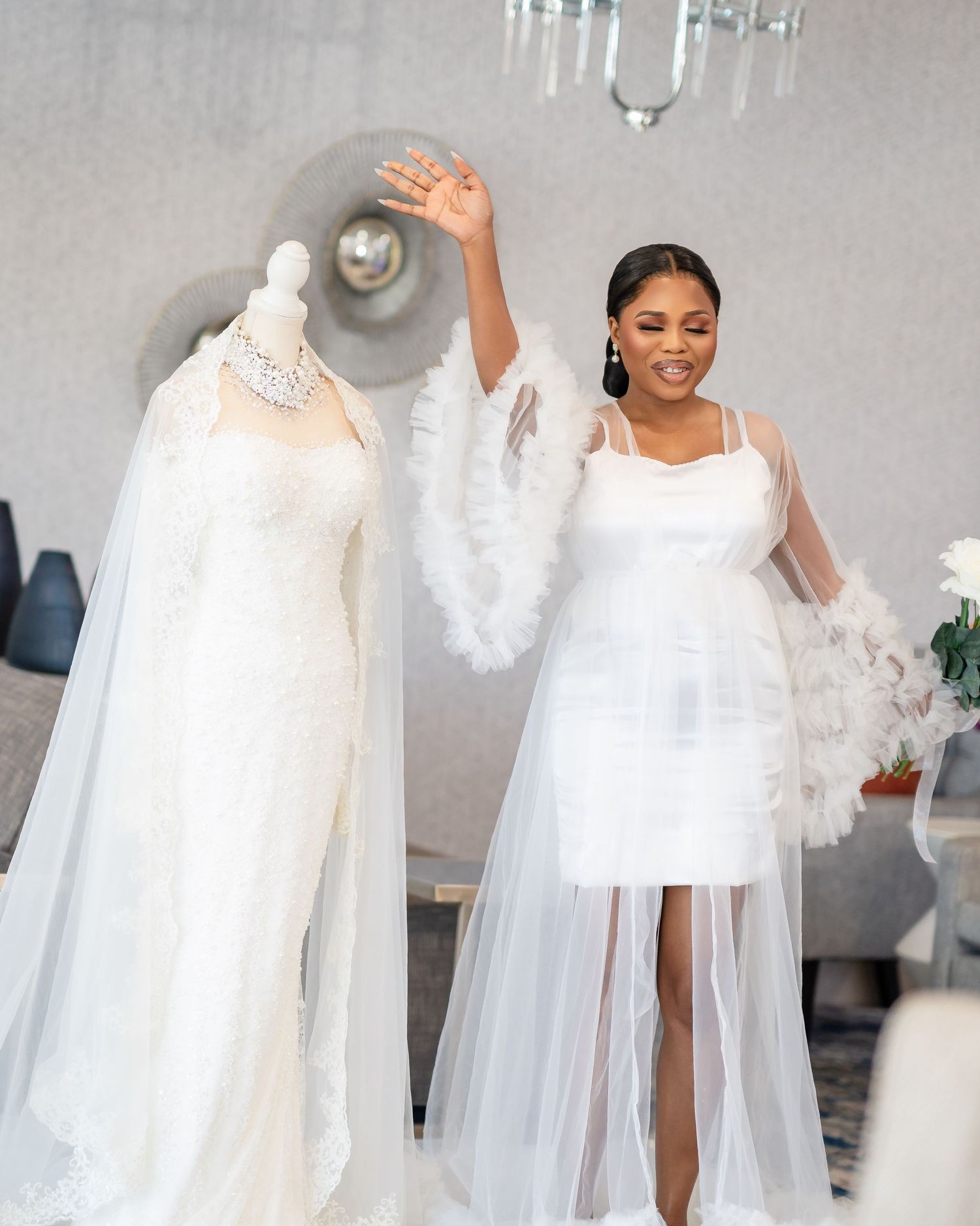 Elegant wedding party in flowing white dresses poses in a light-filled room.