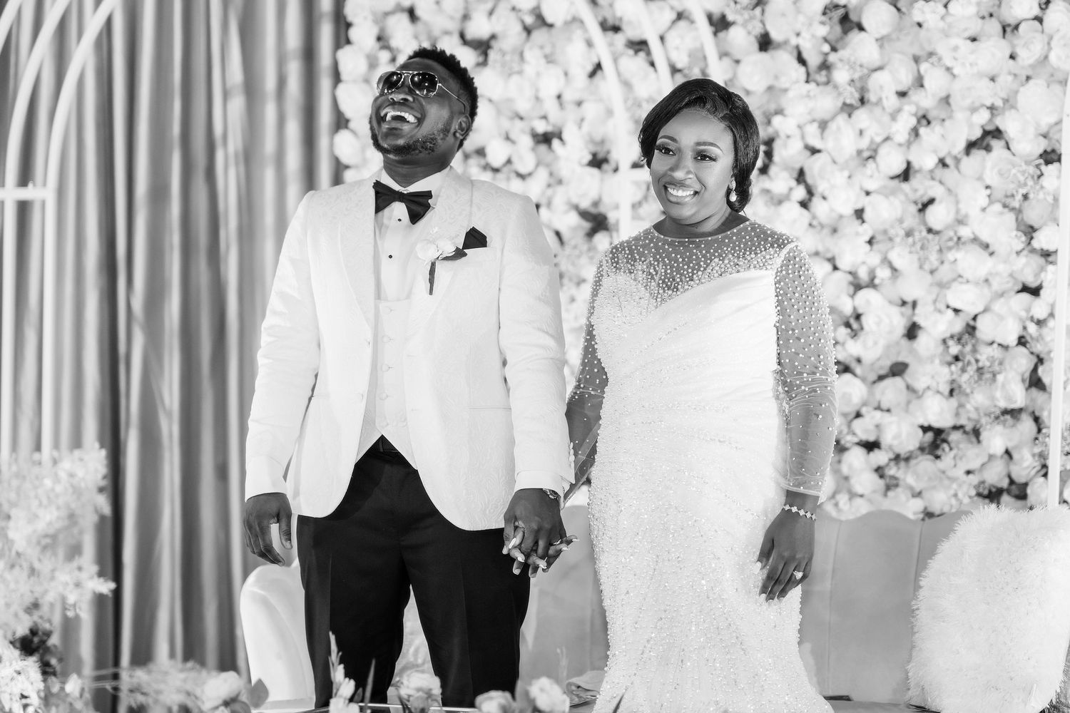 A couple shares a joyful moment at their wedding ceremony in front of a white floral backdrop.