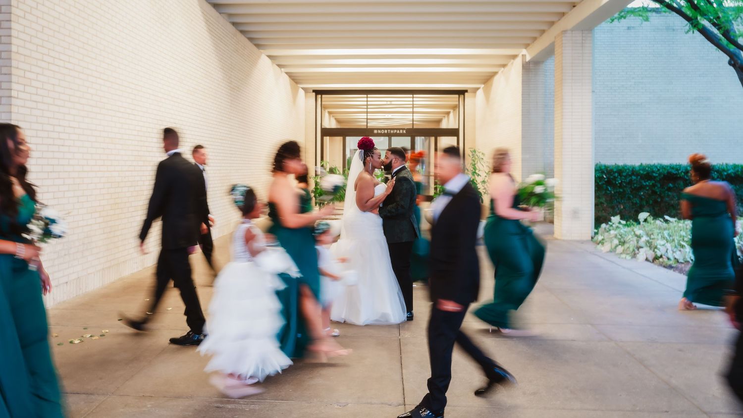 Motion-blurred wedding guests walking through a bright white hallway.