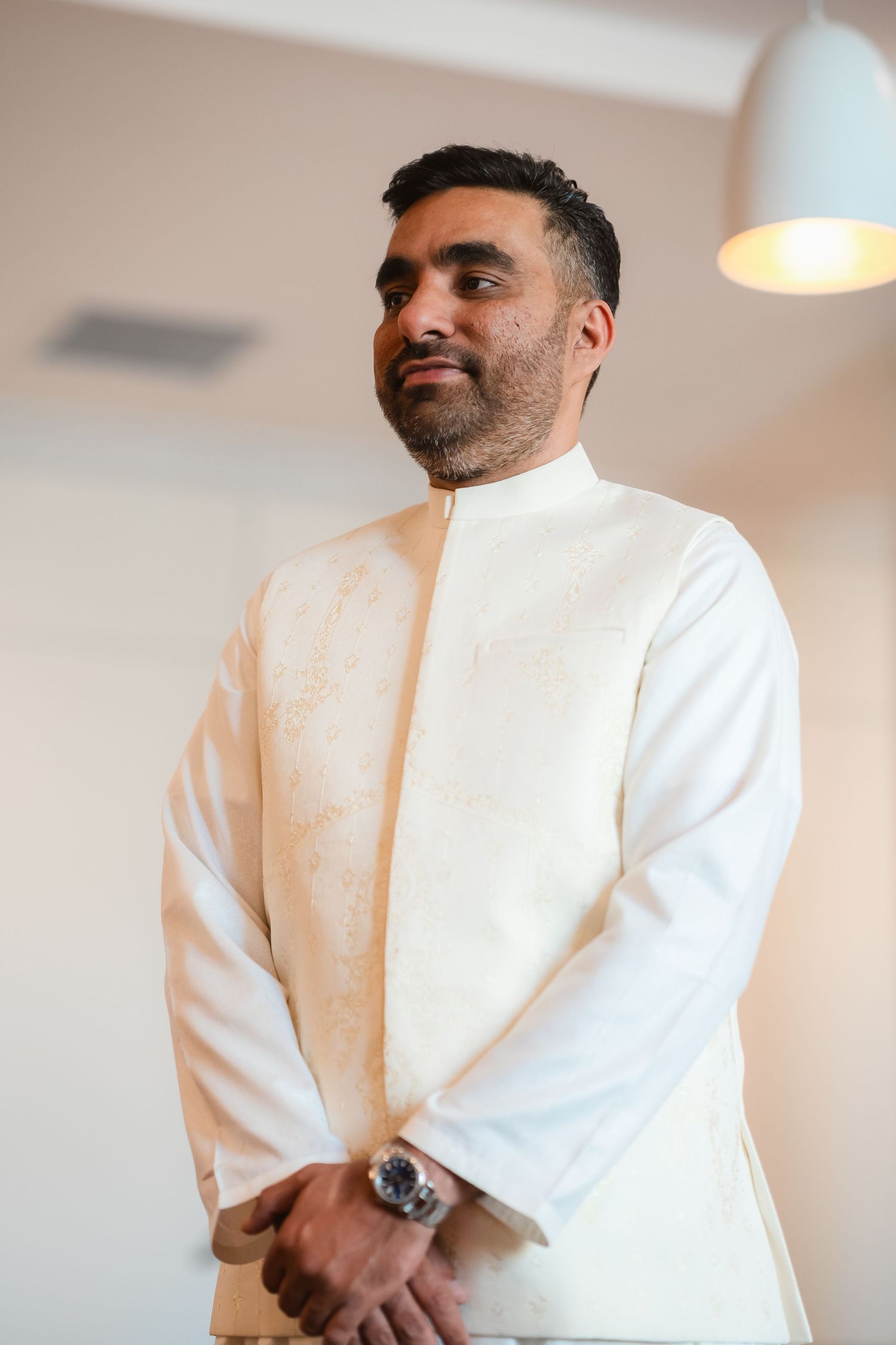 Groom in a crisp white traditional outfit poses against a light background.