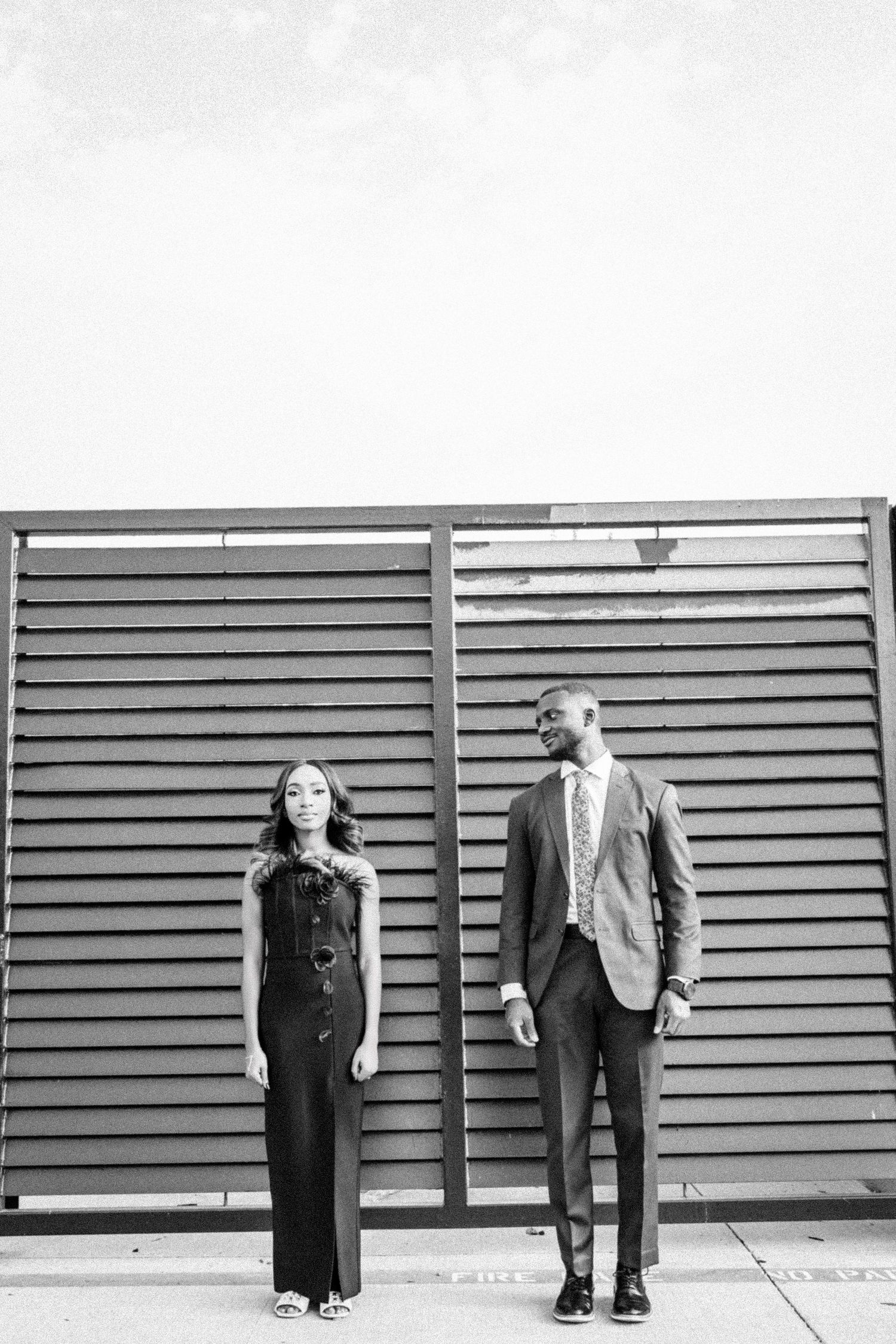 A black and white portrait of a couple in formal wear posing against industrial shutters.