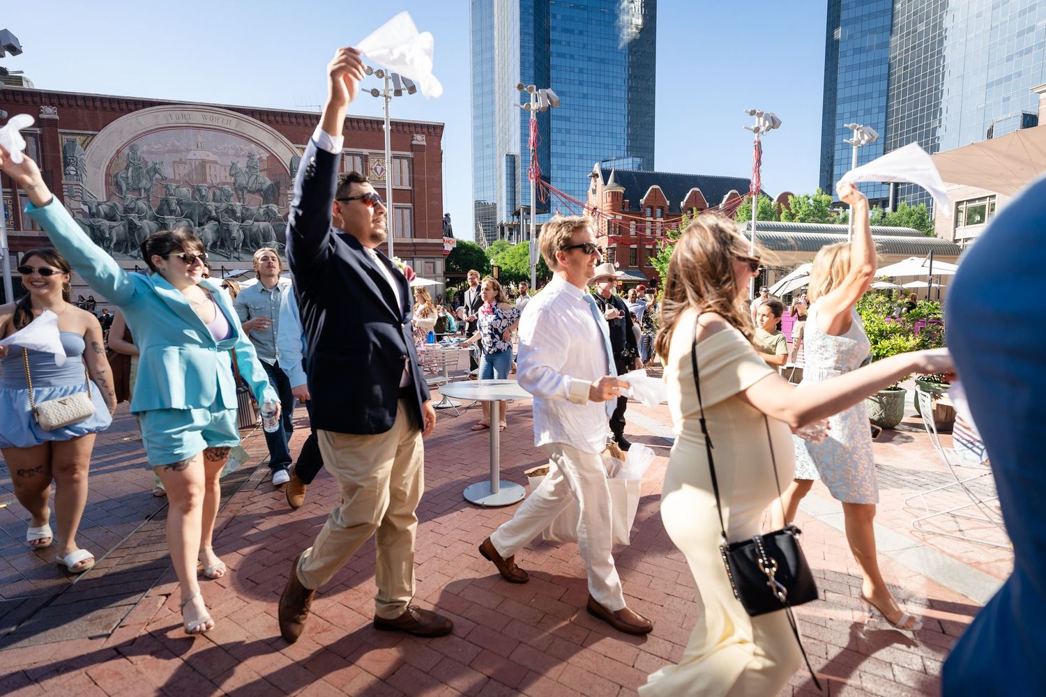 Wedding guests dancing and celebrating outdoors with city buildings visible in the background.