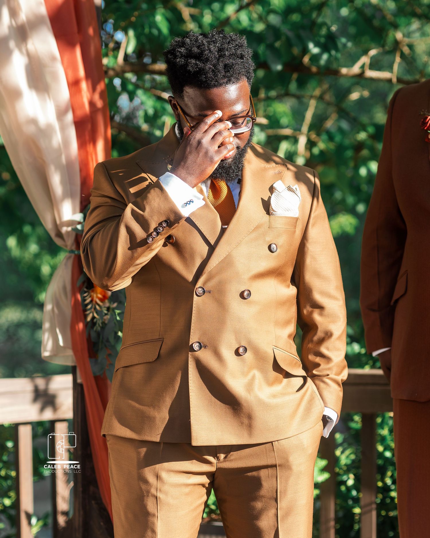 Wedding party member wearing a stylish tan double-breasted suit in an outdoor garden setting.