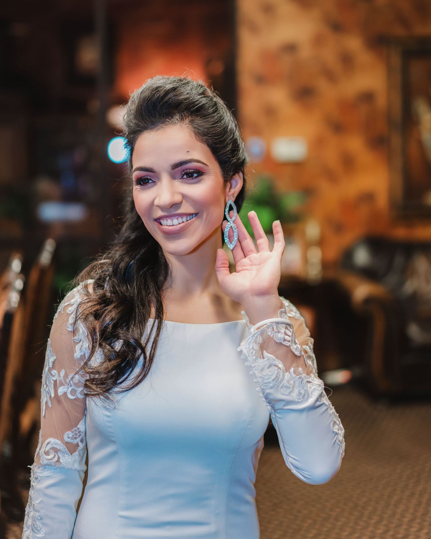 Bride wearing an elegant long-sleeved white dress with lace details smiles joyfully during wedding celebrations.