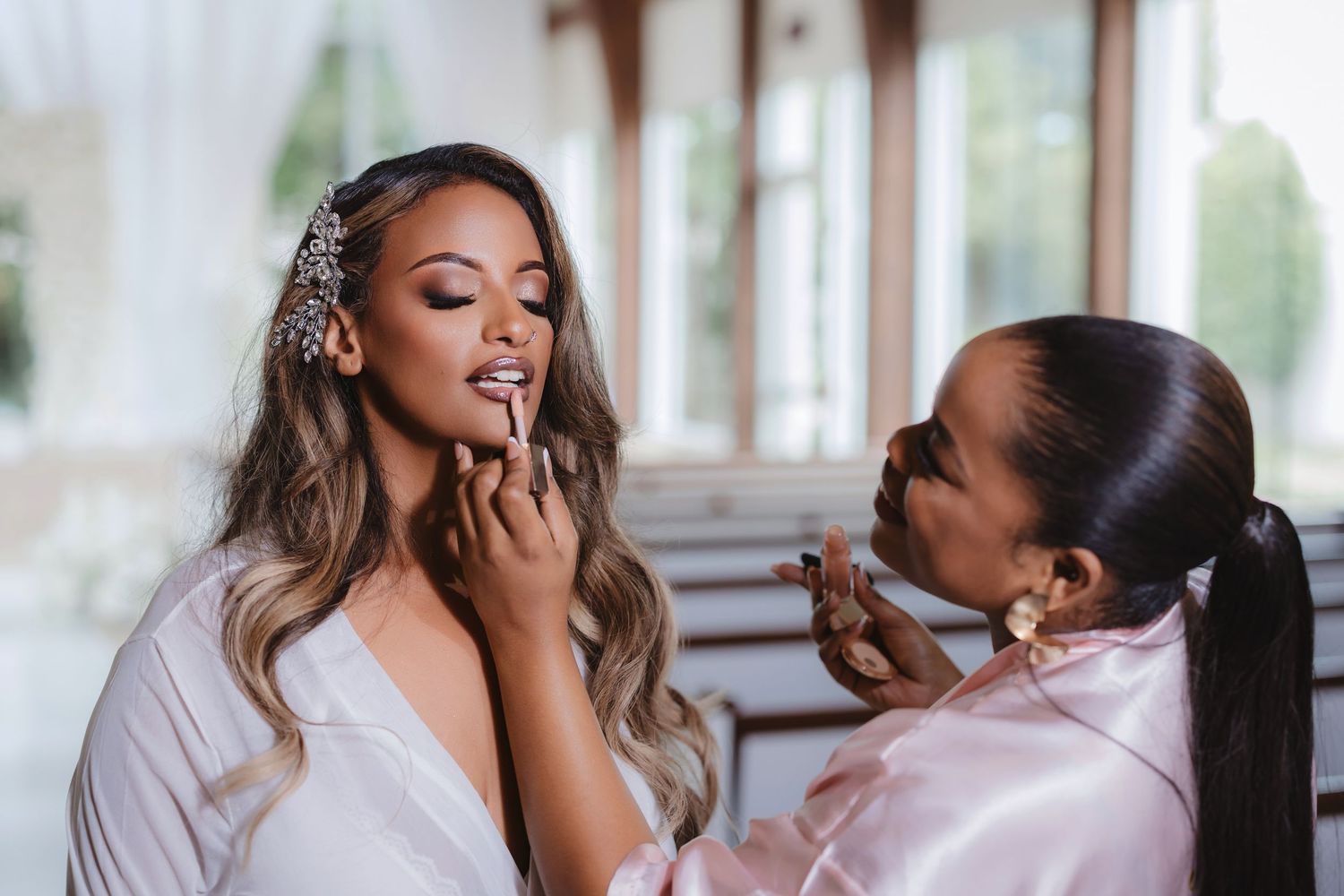 Behind-the-scenes wedding preparation showing makeup application in natural light.