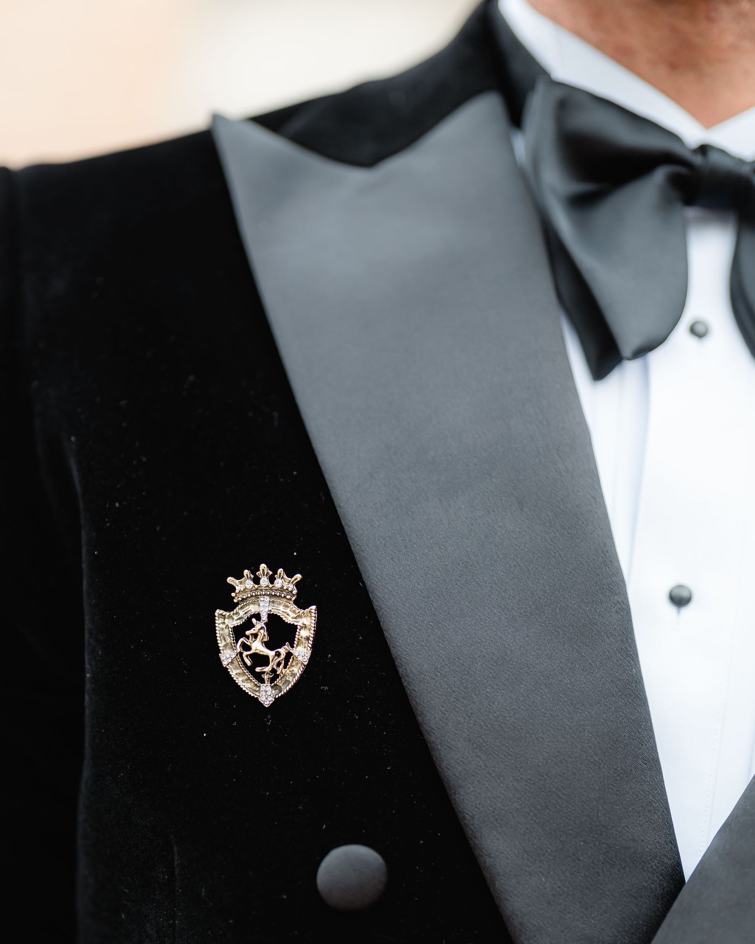 Close-up details of a formal black tuxedo with bow tie and decorative lapel pin.