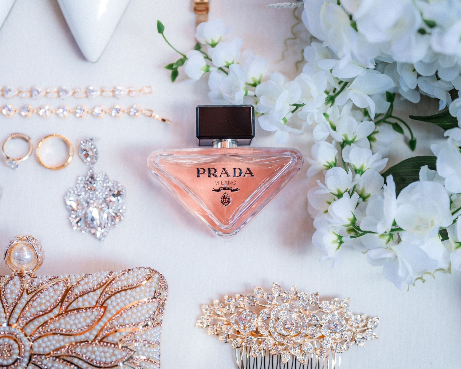 Wedding accessories including rings, perfume, and crystal hair pieces arranged on white surface with delicate flowers.