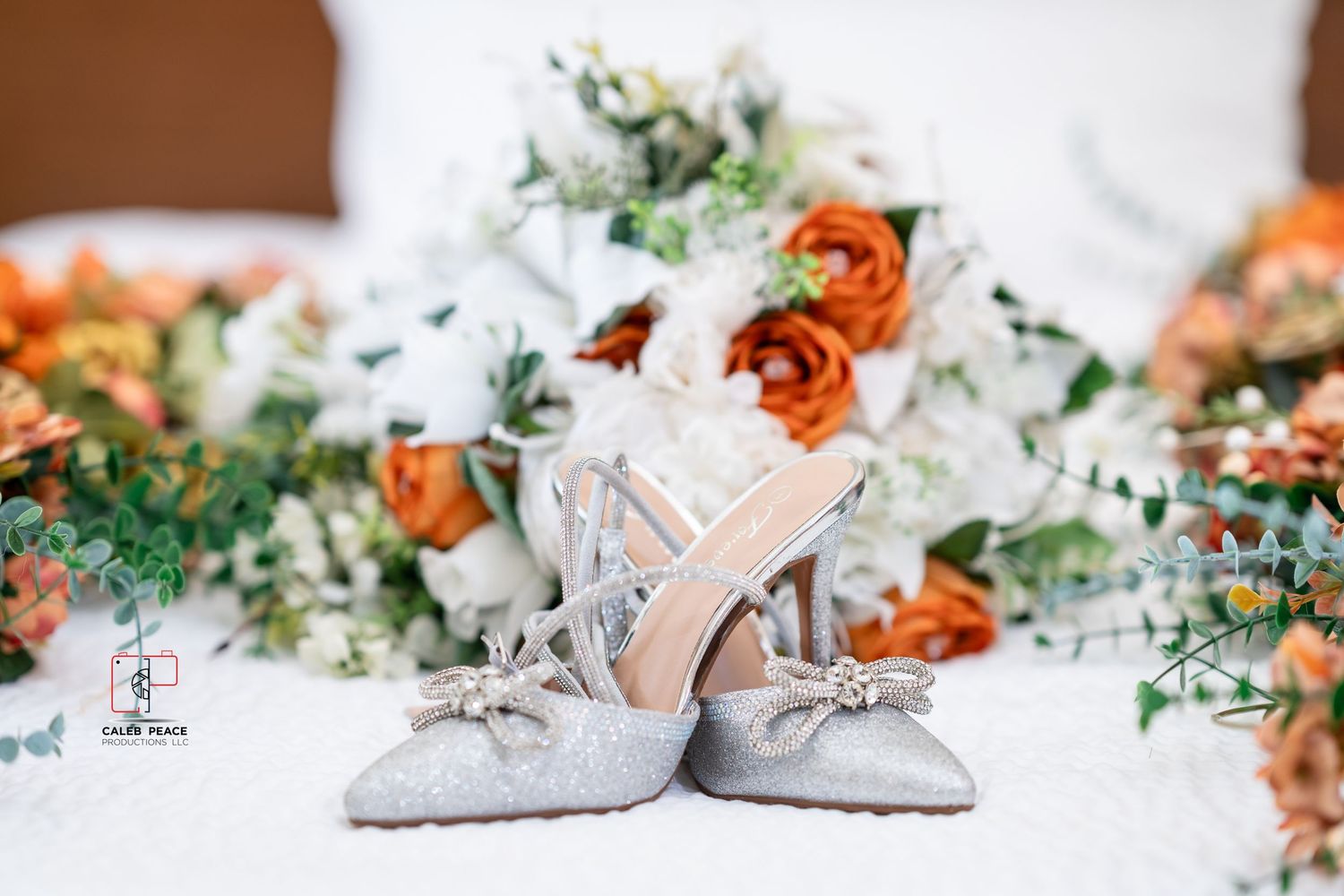 Wedding shoes and floral details with orange and white flowers arranged on a white surface with delicate styling.