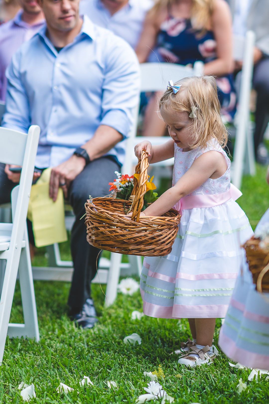 Young flower girls in pink dresses carrying wicker baskets at an outdoor wedding ceremony.