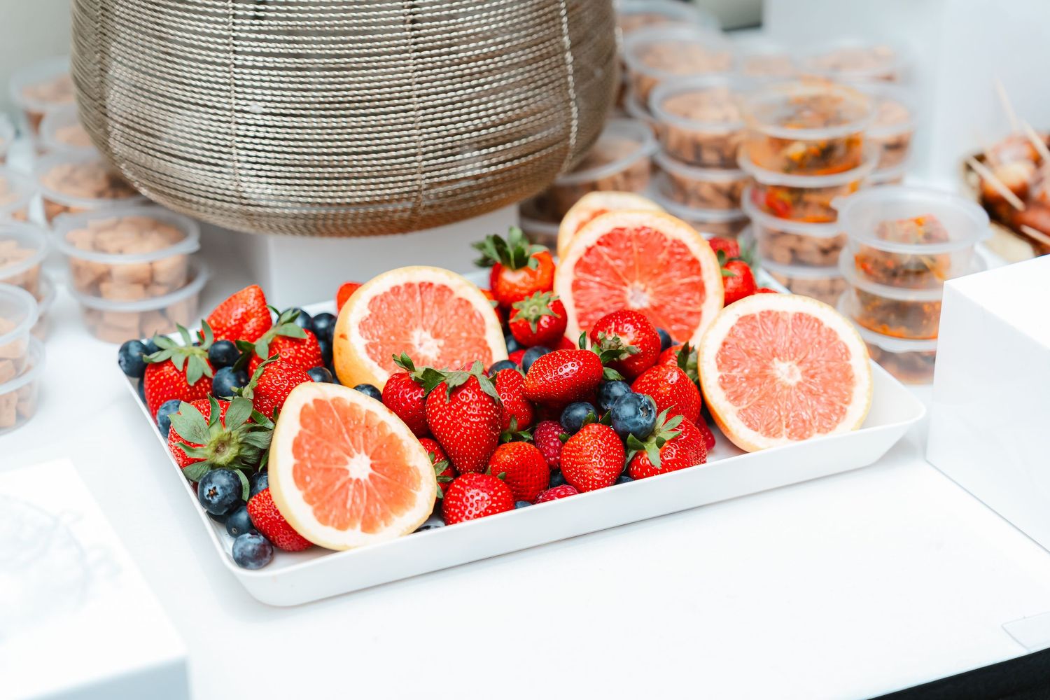 Fresh strawberries and sliced pink grapefruit arranged on white serving plates with glass containers in background.