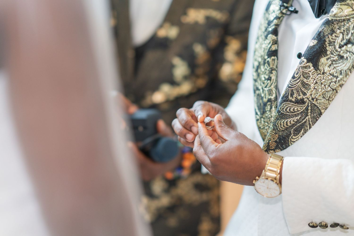 Close-up shot of hands exchanging rings during a wedding ceremony with a gold watch visible.