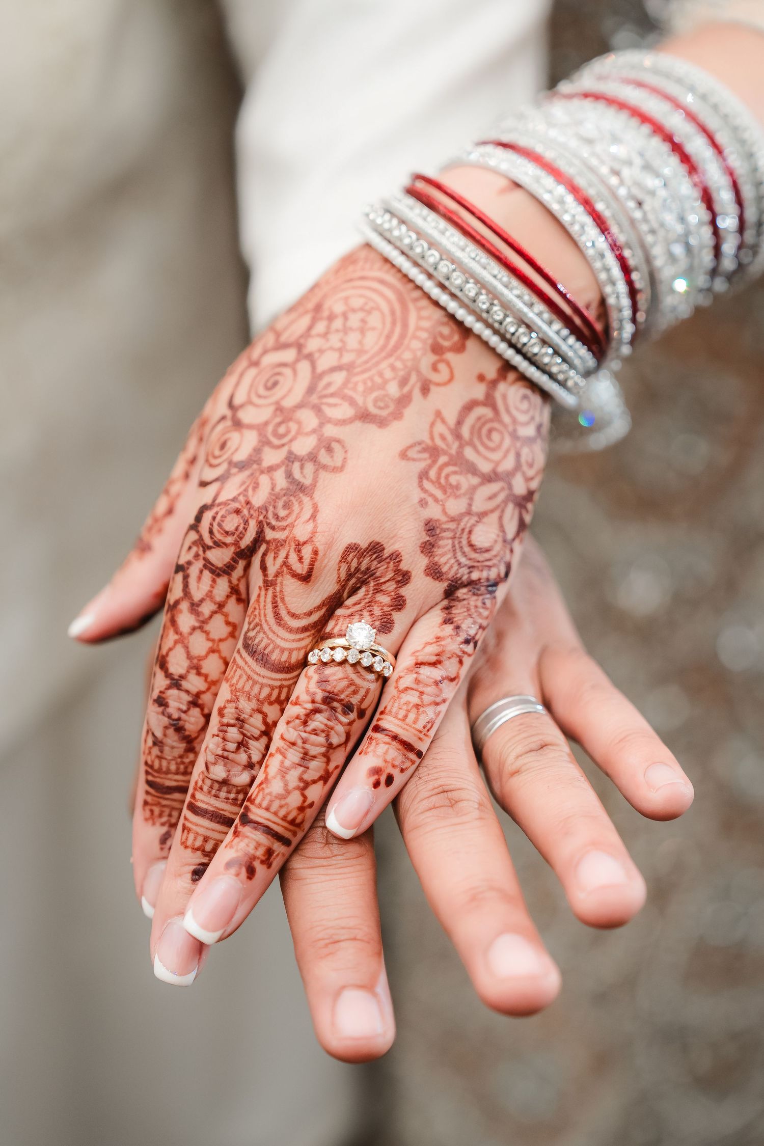 Close-up view of hands adorned with intricate henna designs and traditional red and white bangles.