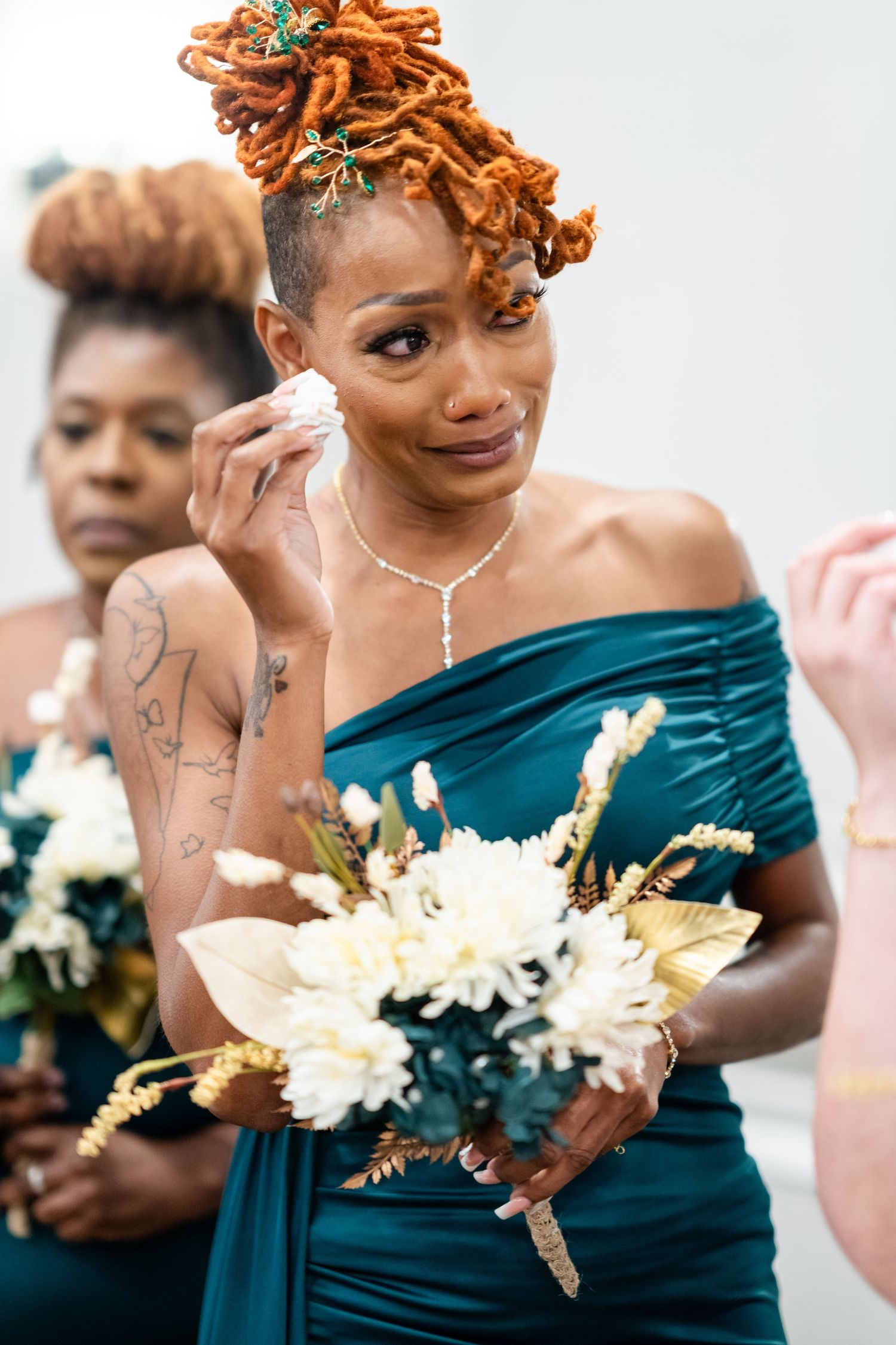 Bridesmaids in teal off-shoulder dresses holding white and gold bouquets.