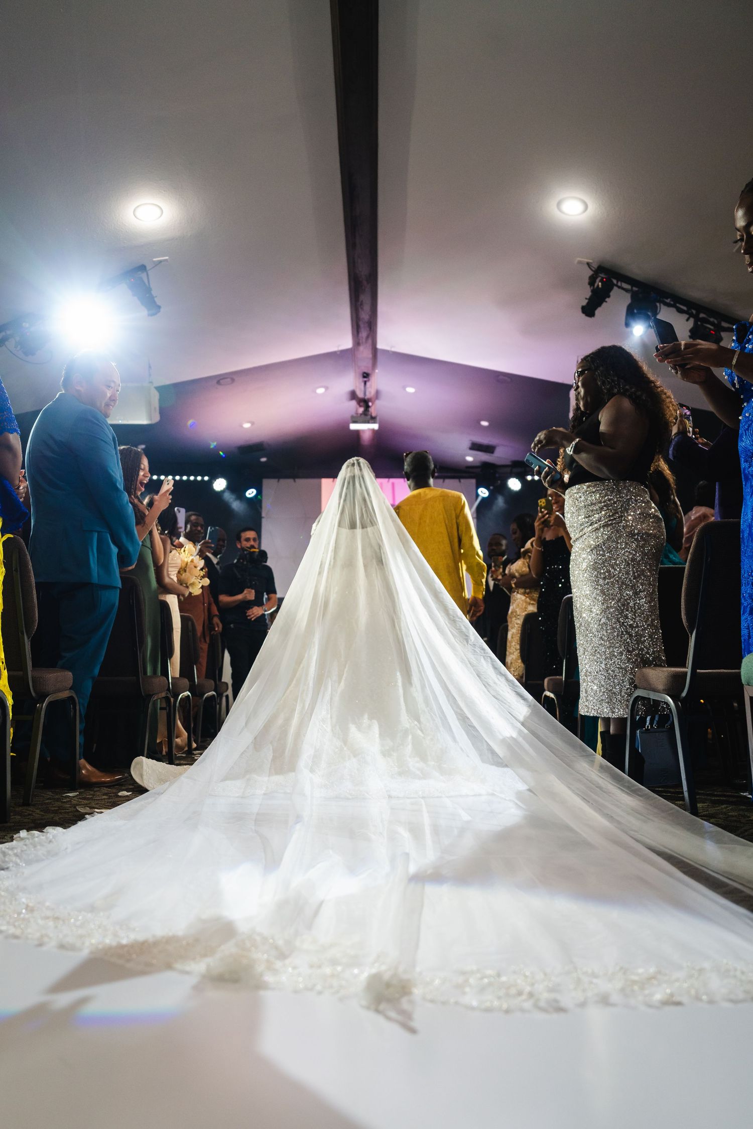 Dramatic low-angle shots of a flowing white wedding gown with cathedral train in a dimly lit venue.