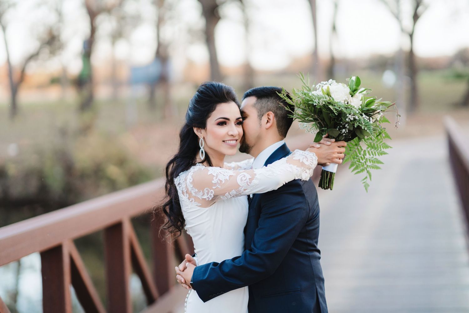 Wedding couple embraces on bridge during outdoor photo session.
