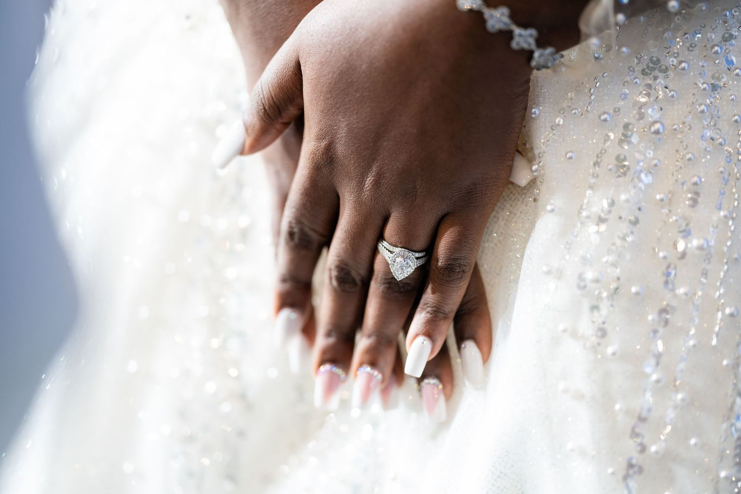 Close-up of hands touching intricate beaded details on white fabric.