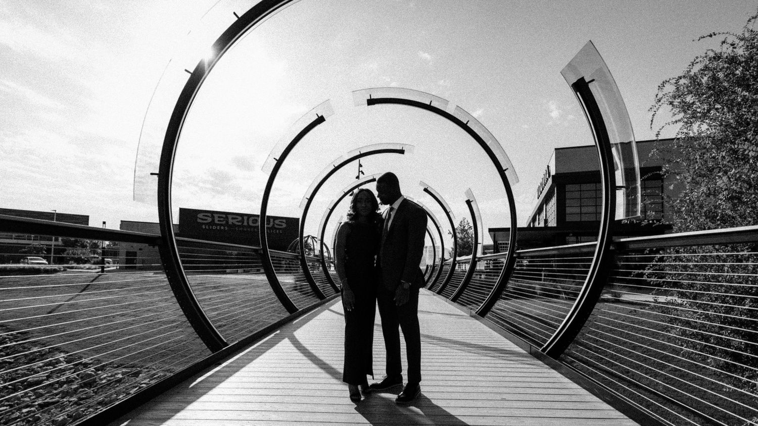 A black and white panoramic collage showing people walking through curved architectural tunnels and passageways.