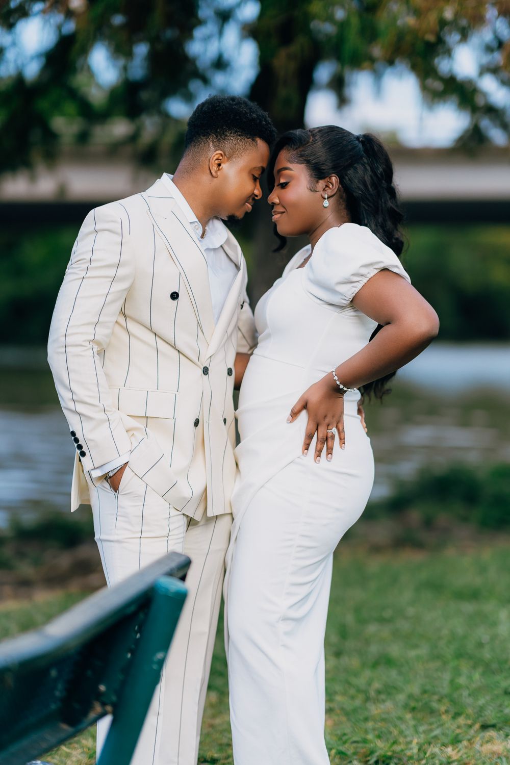 A romantic couple in white formal attire embrace by a waterfront setting during a photo session.