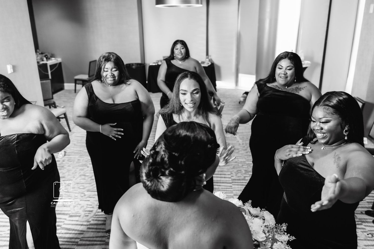 A wedding party in black dresses reacts joyfully during a candid moment.