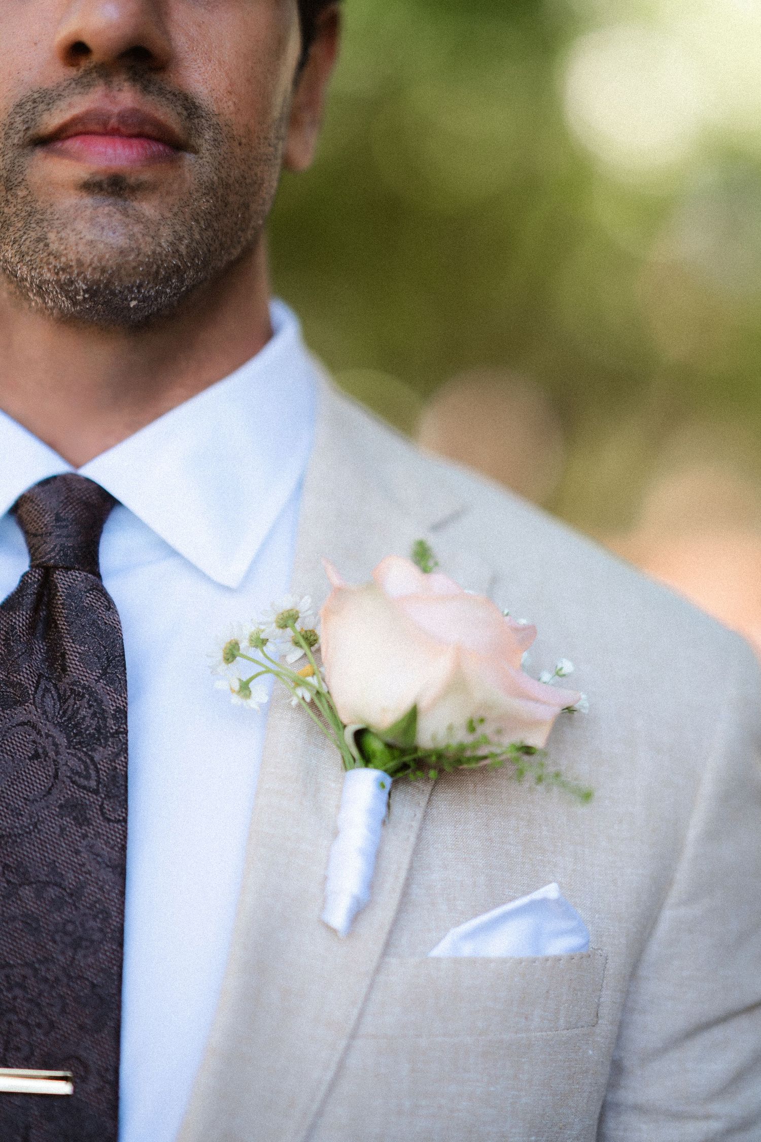 Close-up details of groomsmen wearing light gray suits with pink rose boutonnieres.
