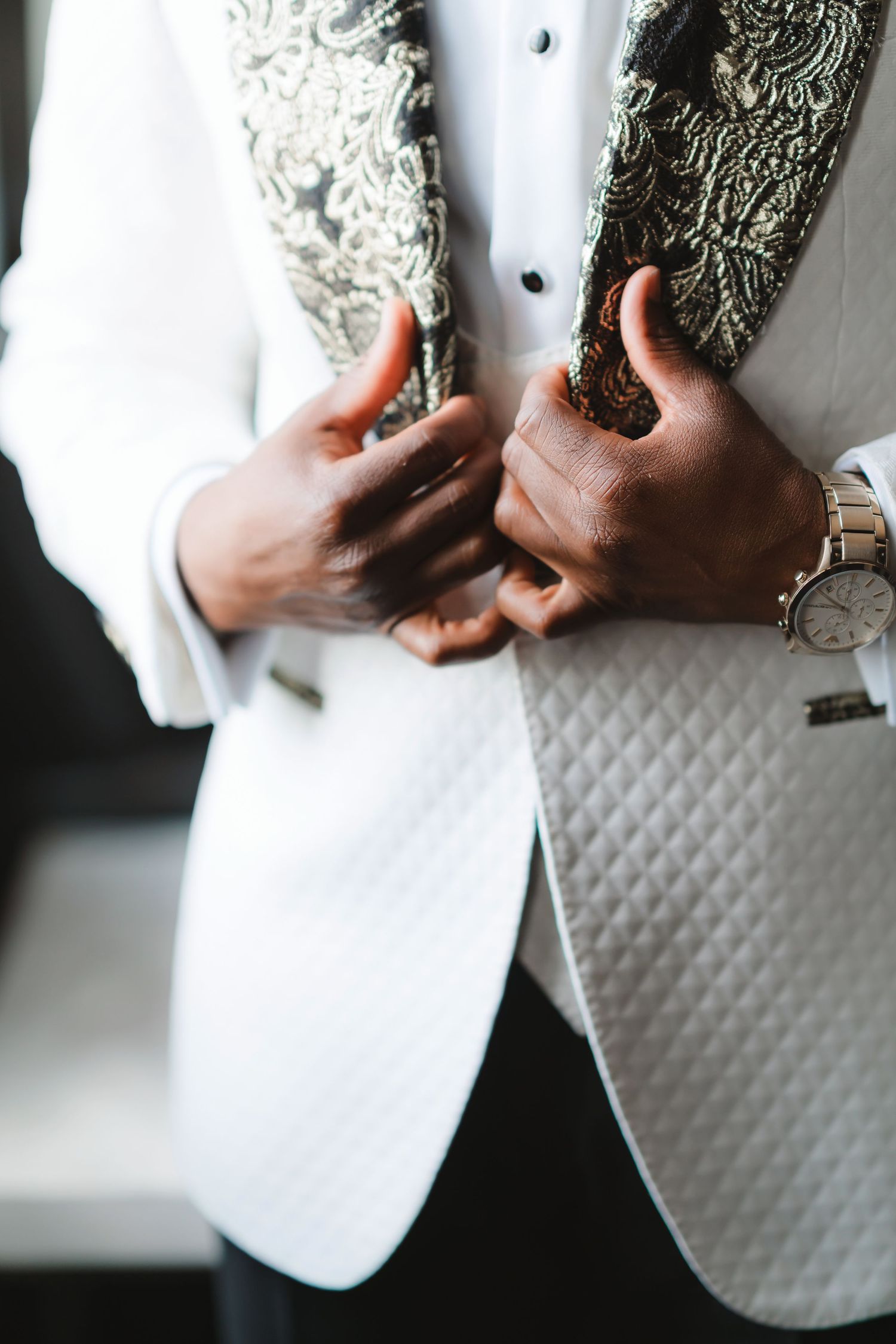 Close-up details of a white tuxedo jacket with intricate embroidered details and buttons.