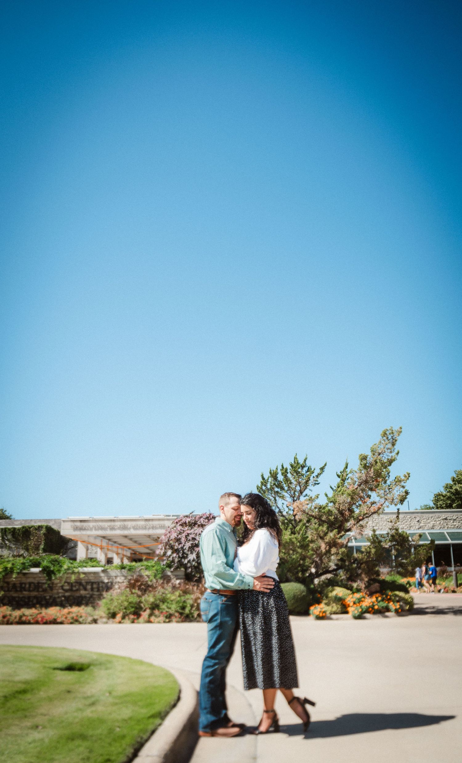 A couple shares a romantic moment together in a garden setting with clear blue skies on a sunny day.