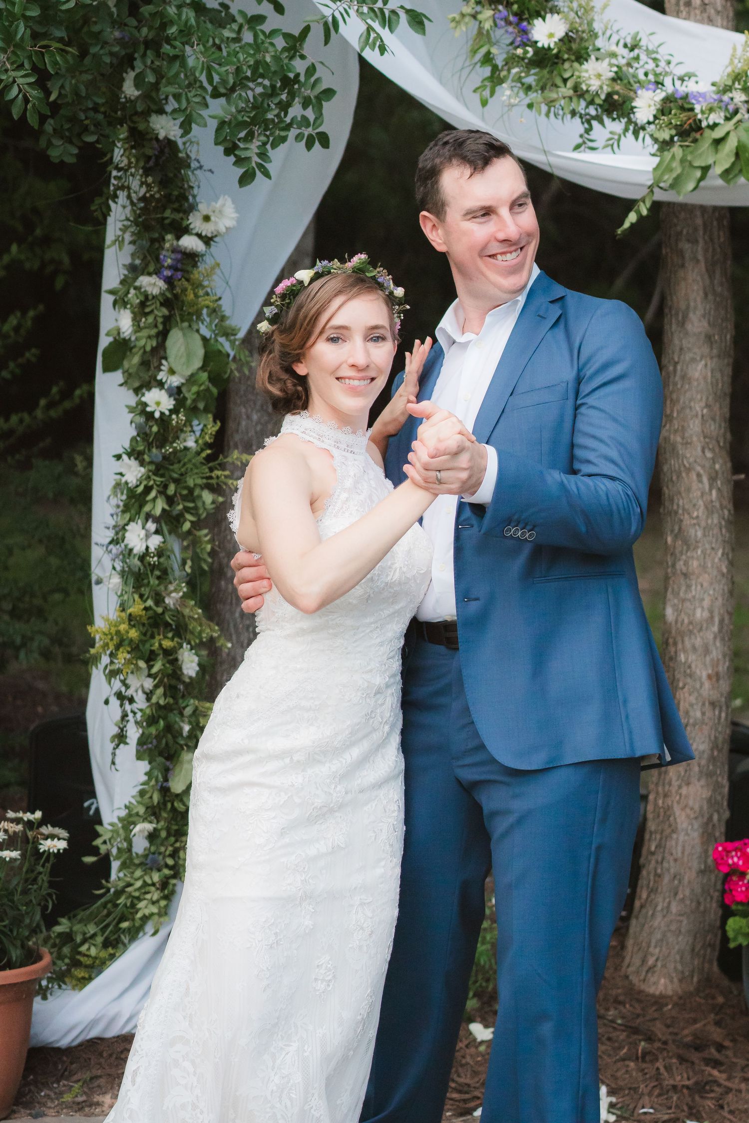 A couple in wedding attire dances and poses together under trees and white fabric during an outdoor celebration.