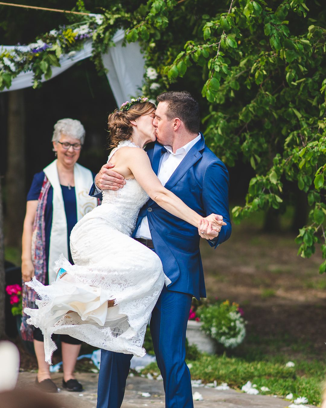 A joyful wedding ceremony kiss captured under a greenery-adorned white fabric arch.