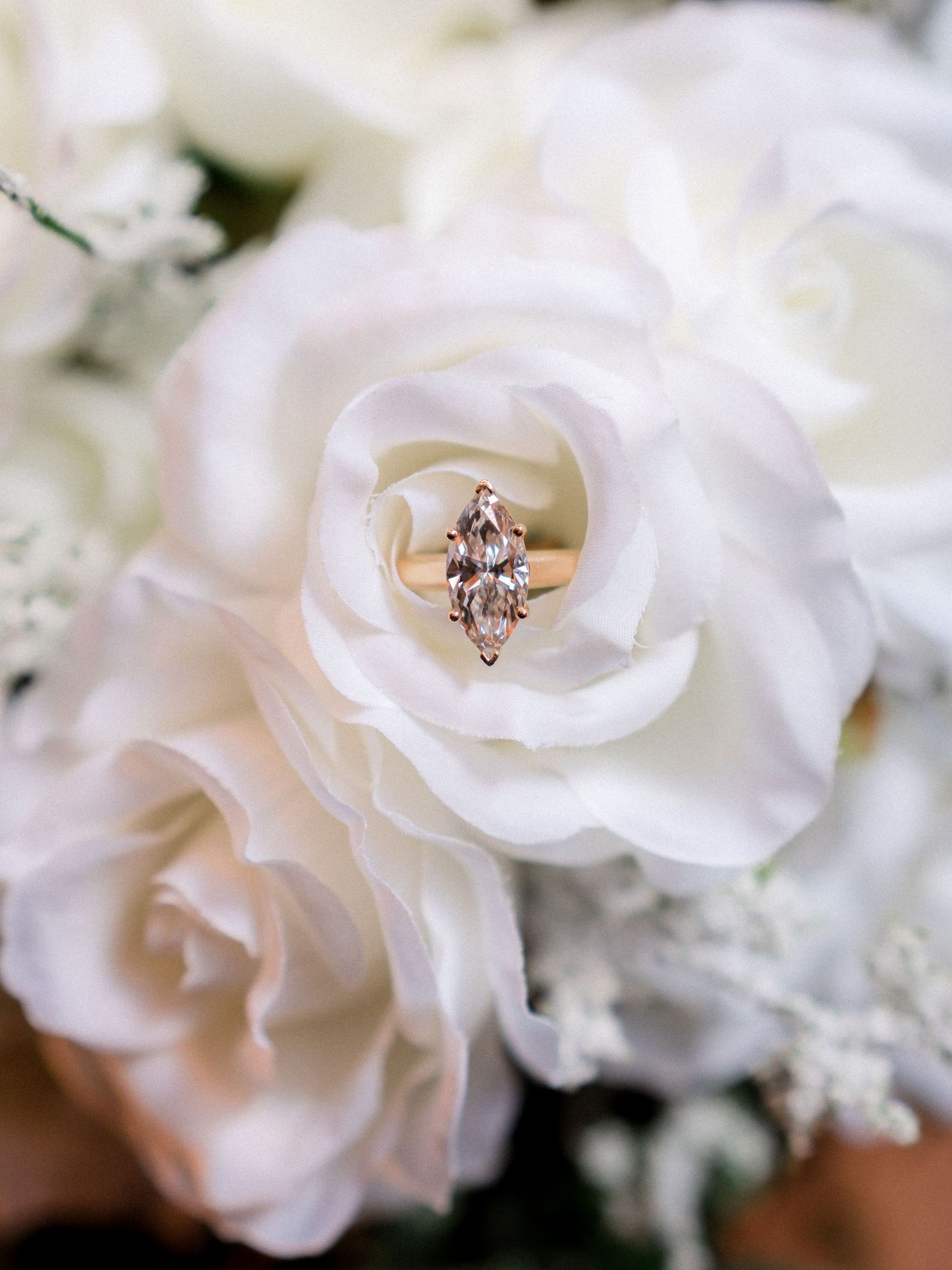 A series of delicate white roses and floral arrangements with an engagement ring in soft focus.