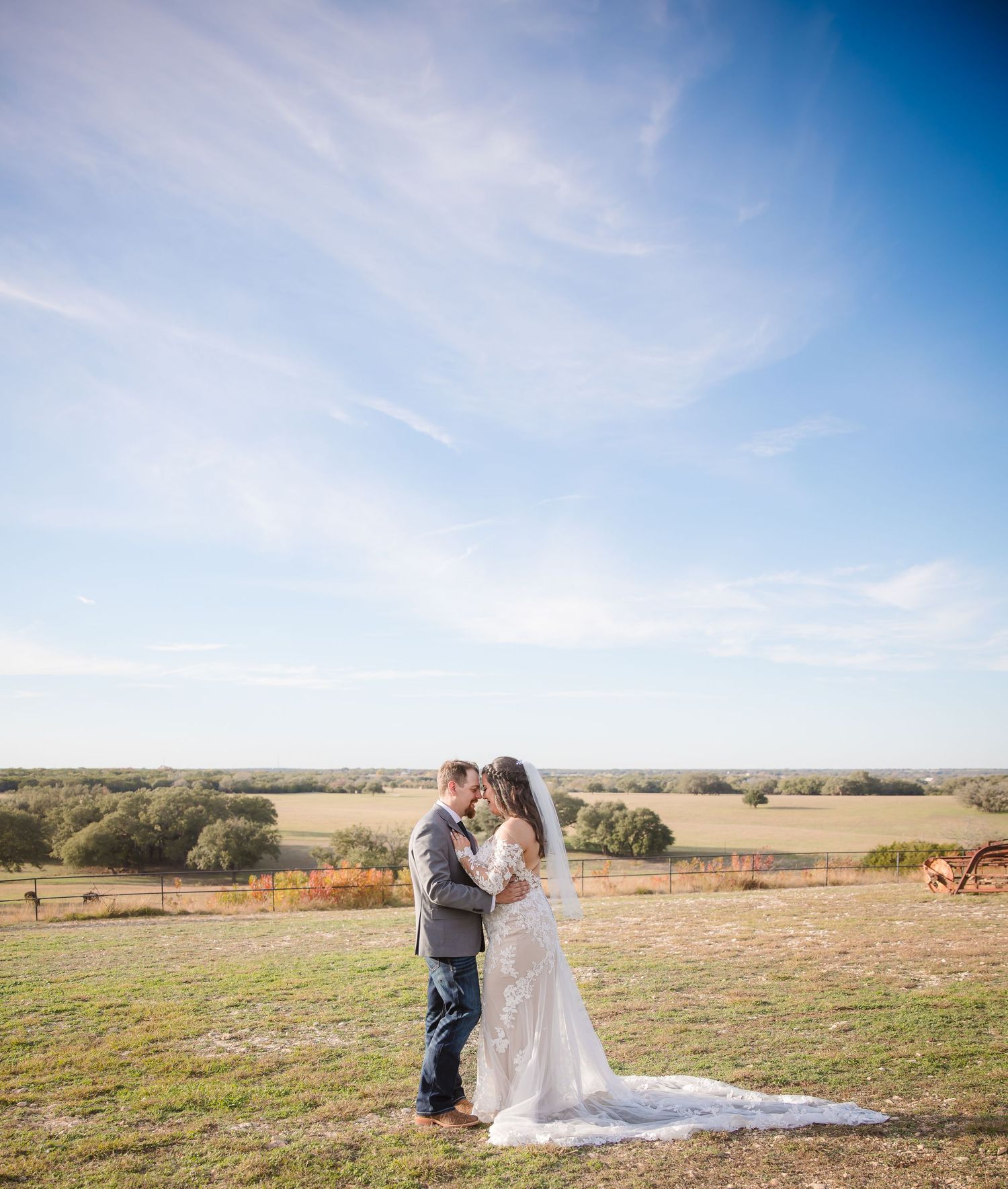 A wedding couple shares an intimate moment in an open field under bright blue skies.