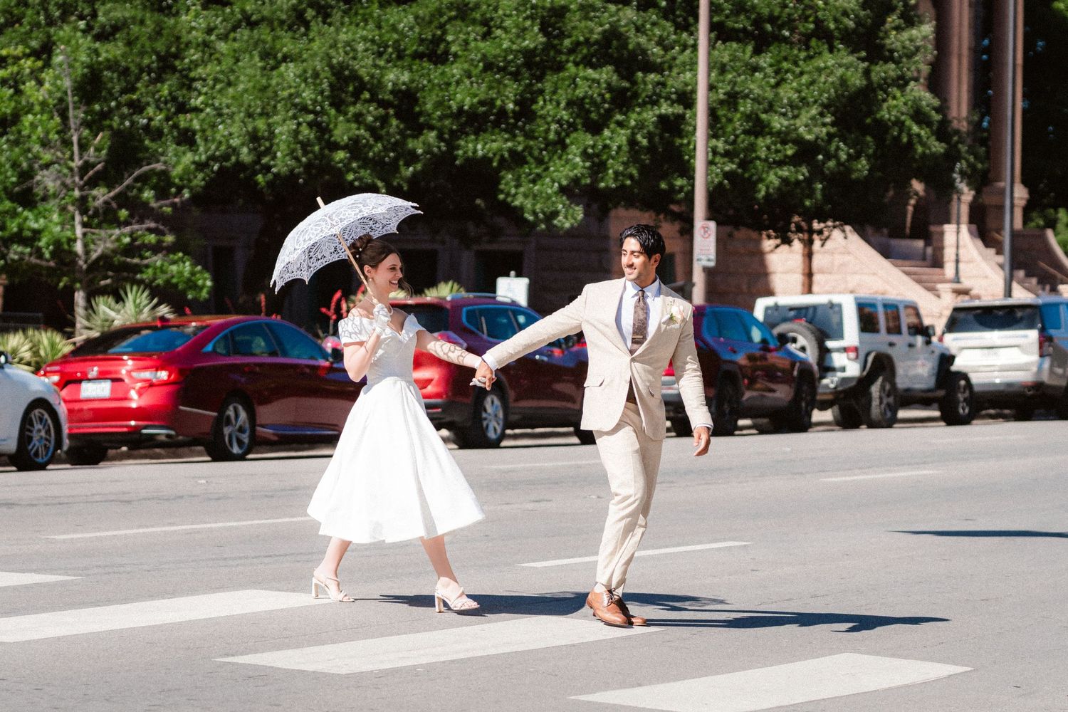 A person in a white dress twirls gracefully in a parking lot on a sunny day.