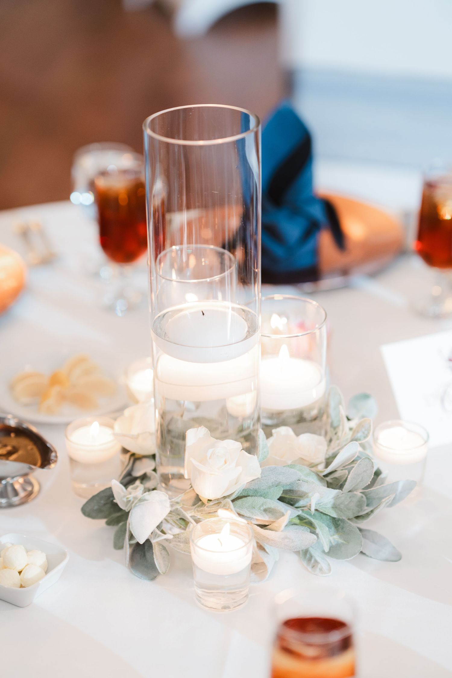Wedding reception table decorated with glass candle holders and delicate eucalyptus leaves.