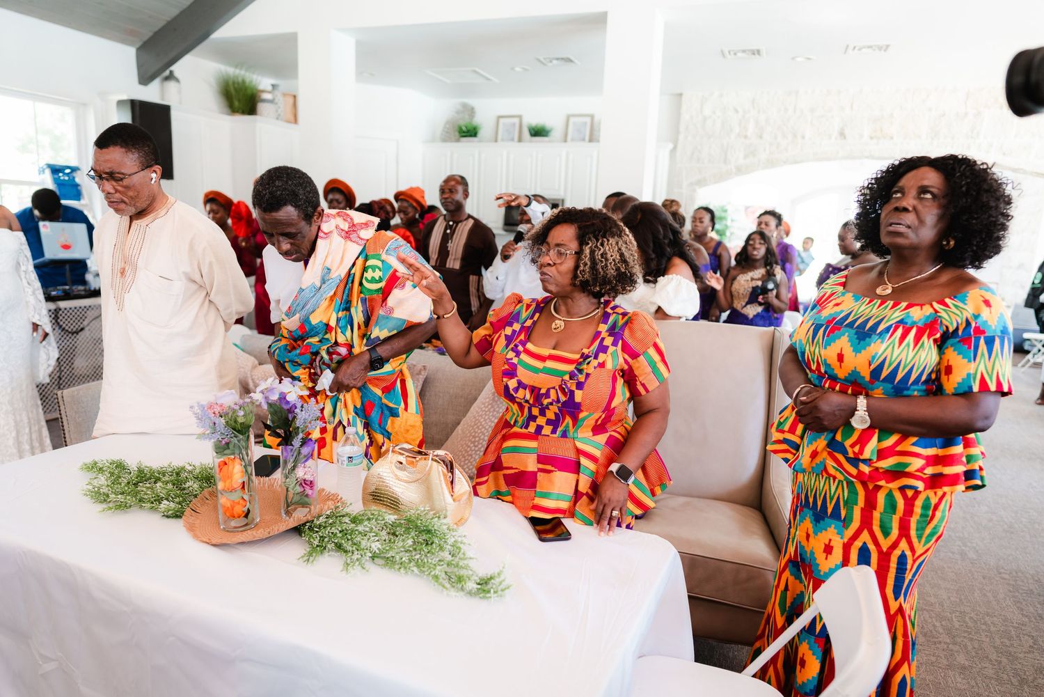 Group celebration in a modern white room with people wearing vibrant traditional attire.