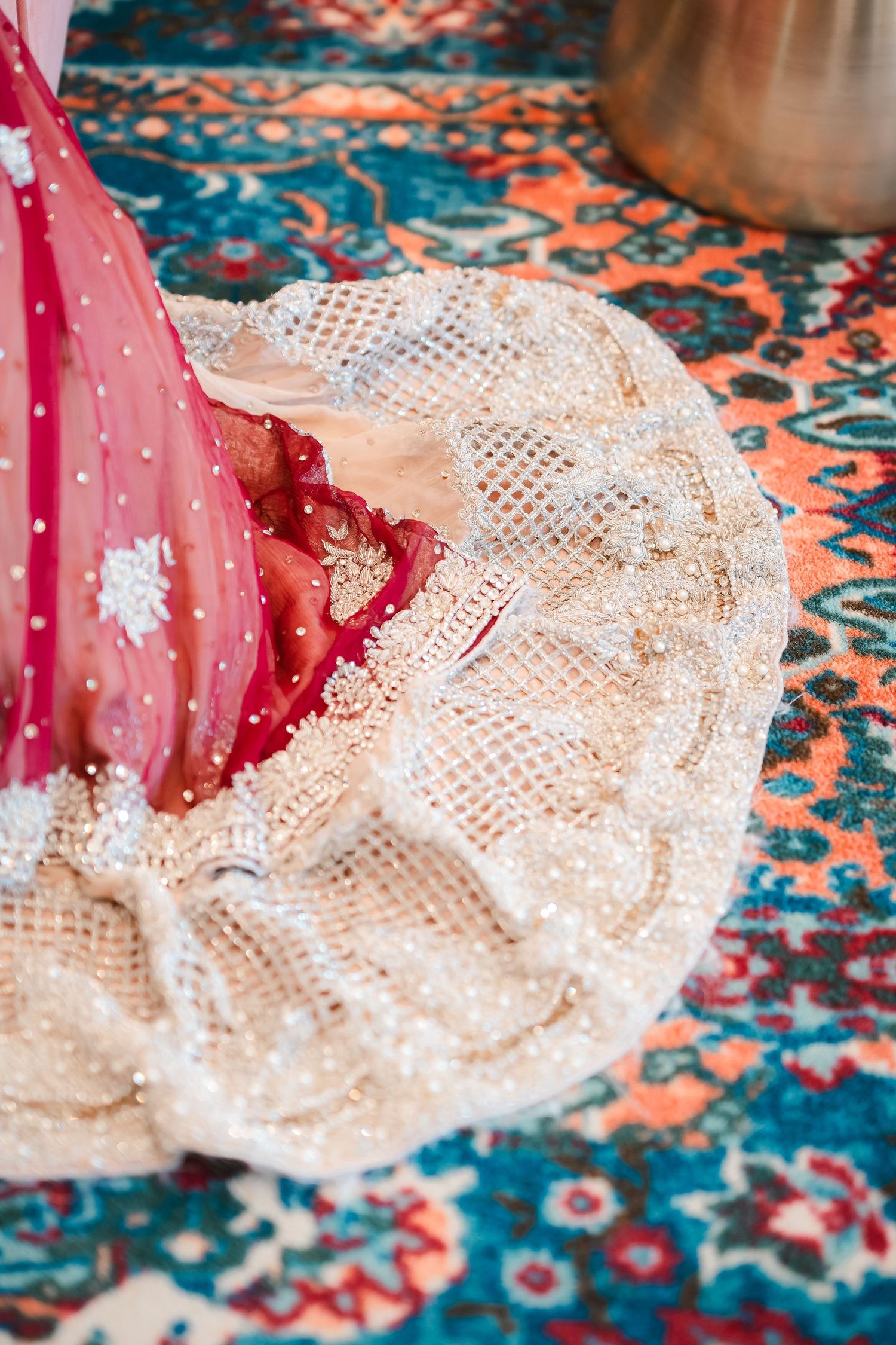 Detail shot of an ornate white and red bridal dress with delicate beadwork on a patterned carpet.