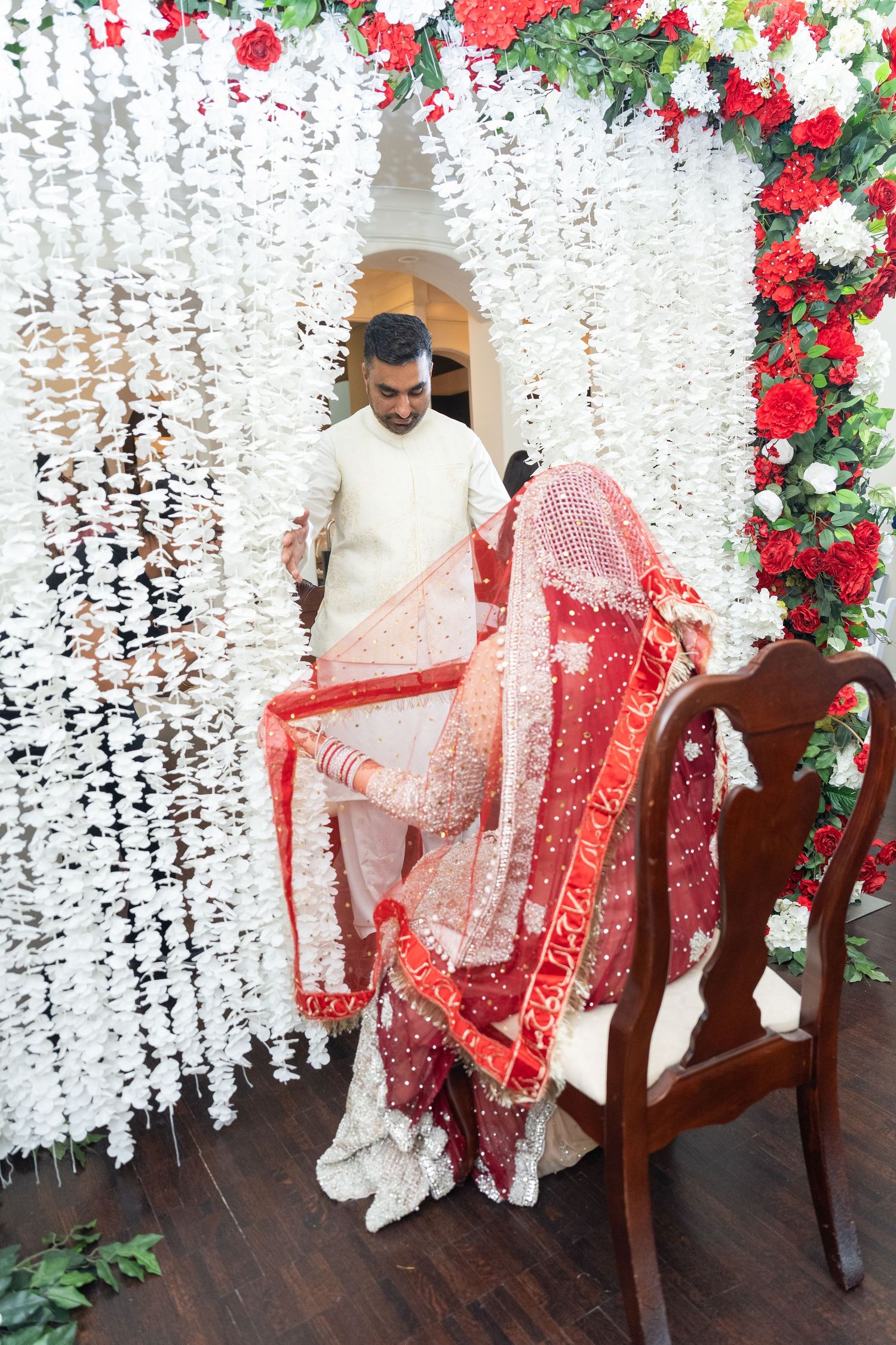 Wedding ceremony space decorated with hanging white floral strands and red rose accents.