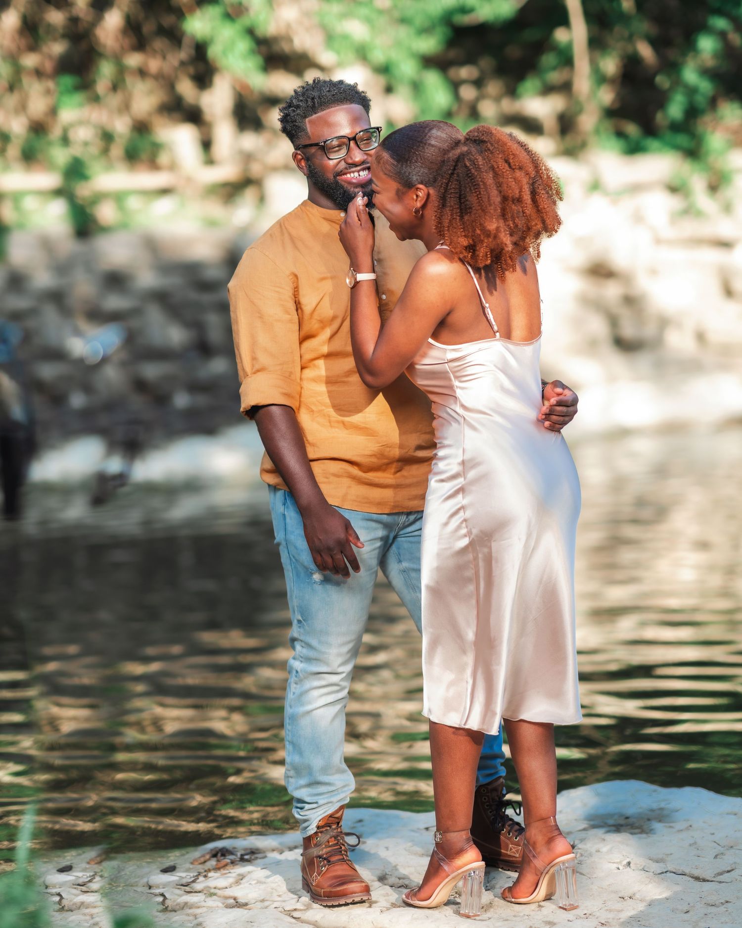 A couple shares a romantic moment by the water's edge on a sunny day.