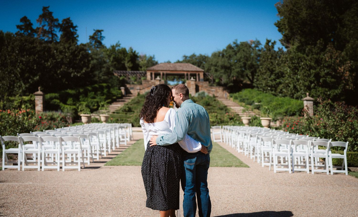 A scenic outdoor wedding venue with rows of white chairs along a stone path surrounded by greenery.