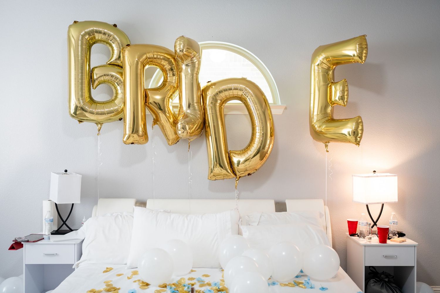 Gold balloon letters spell 'BRIDE' against a white wall with elegant decor and lighting.