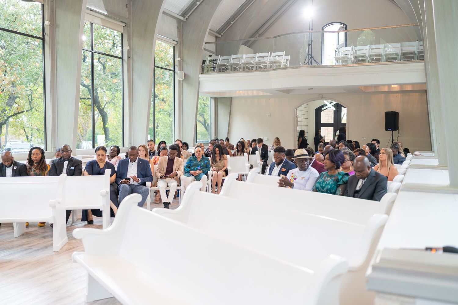 Wedding guests seated in white chairs inside bright, modern chapel venue.