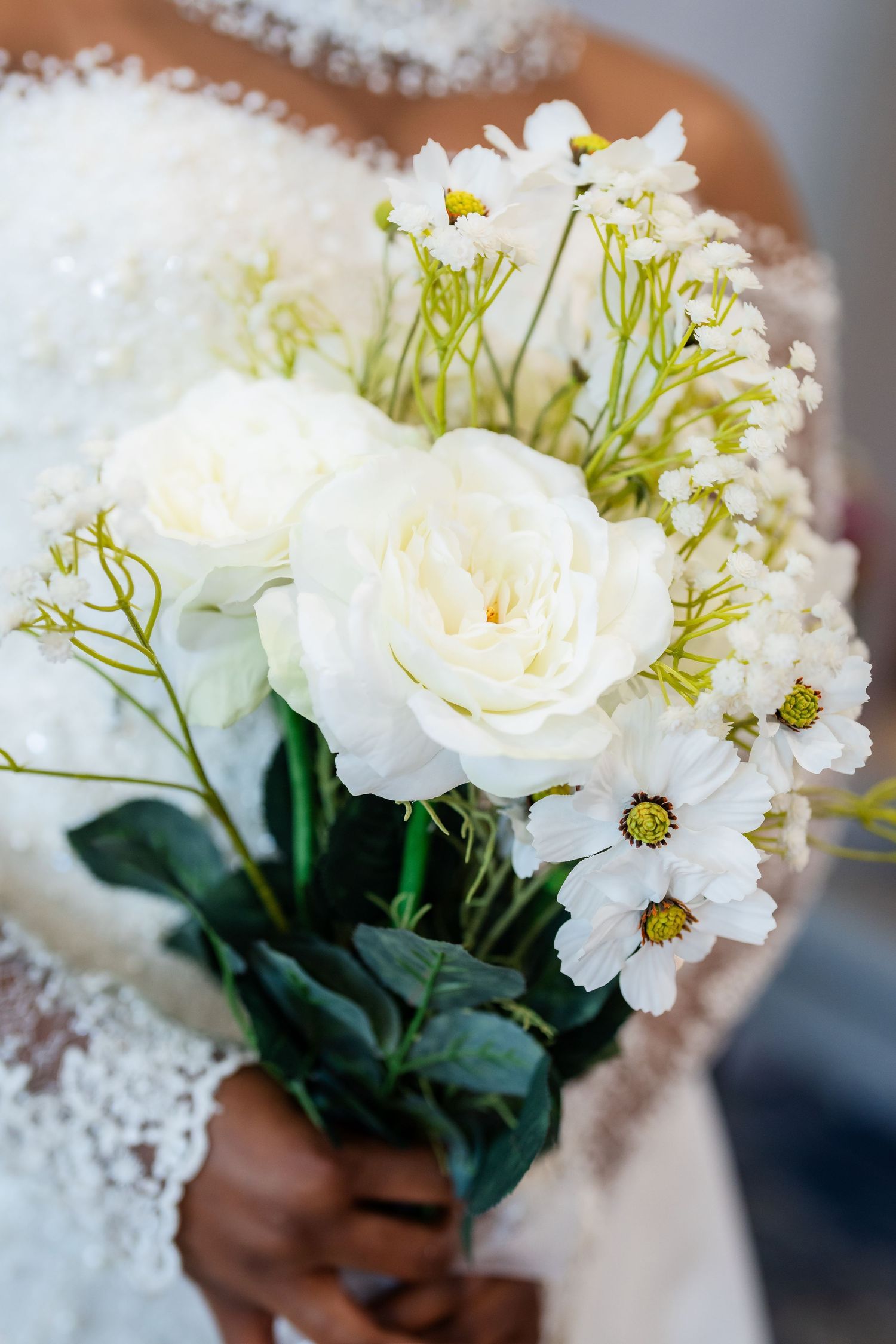 An elegant white wedding bouquet featuring roses and daisies with delicate baby's breath accents.