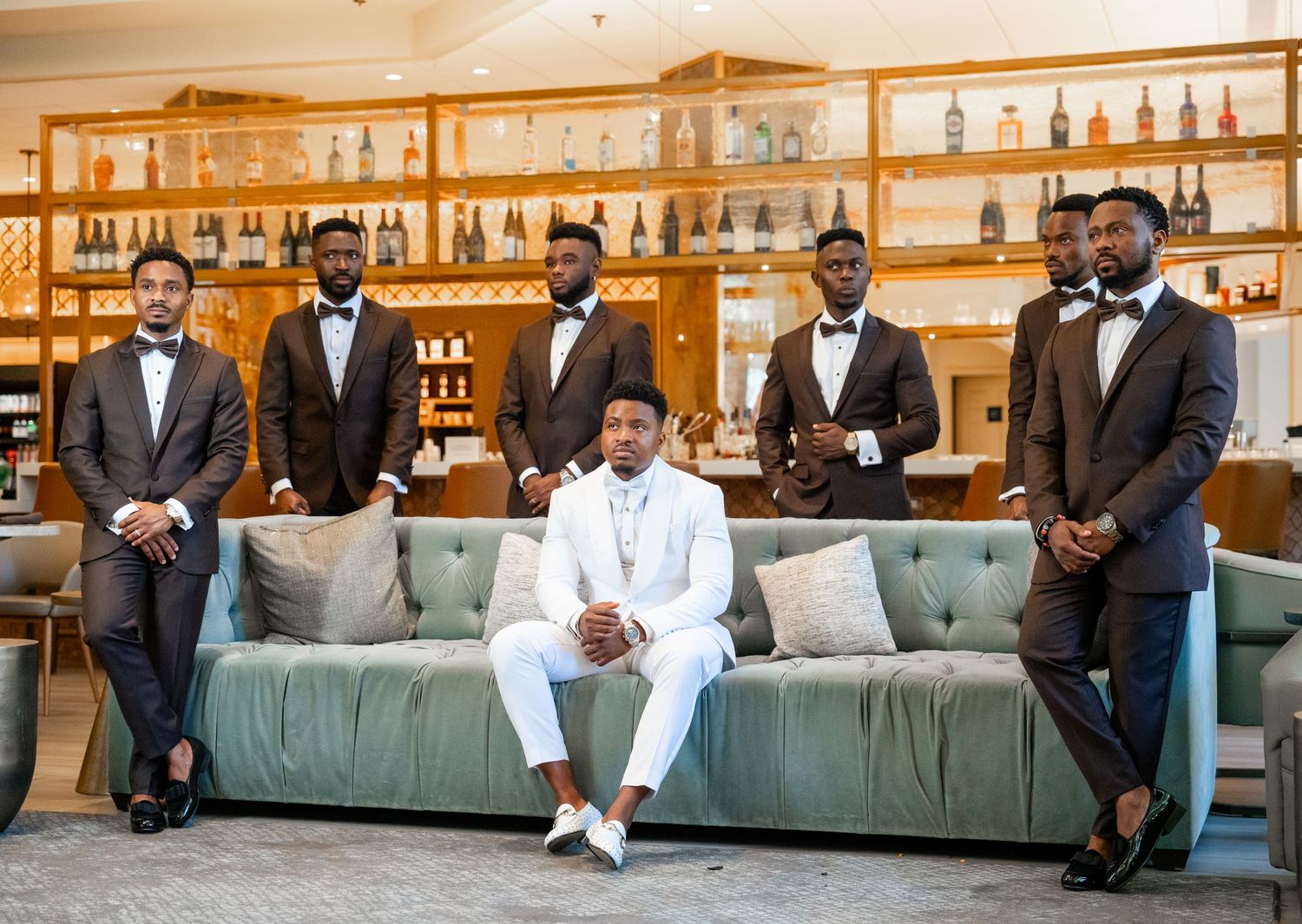 Groomsmen in formal attire pose together on a modern couch in an elegant venue setting.