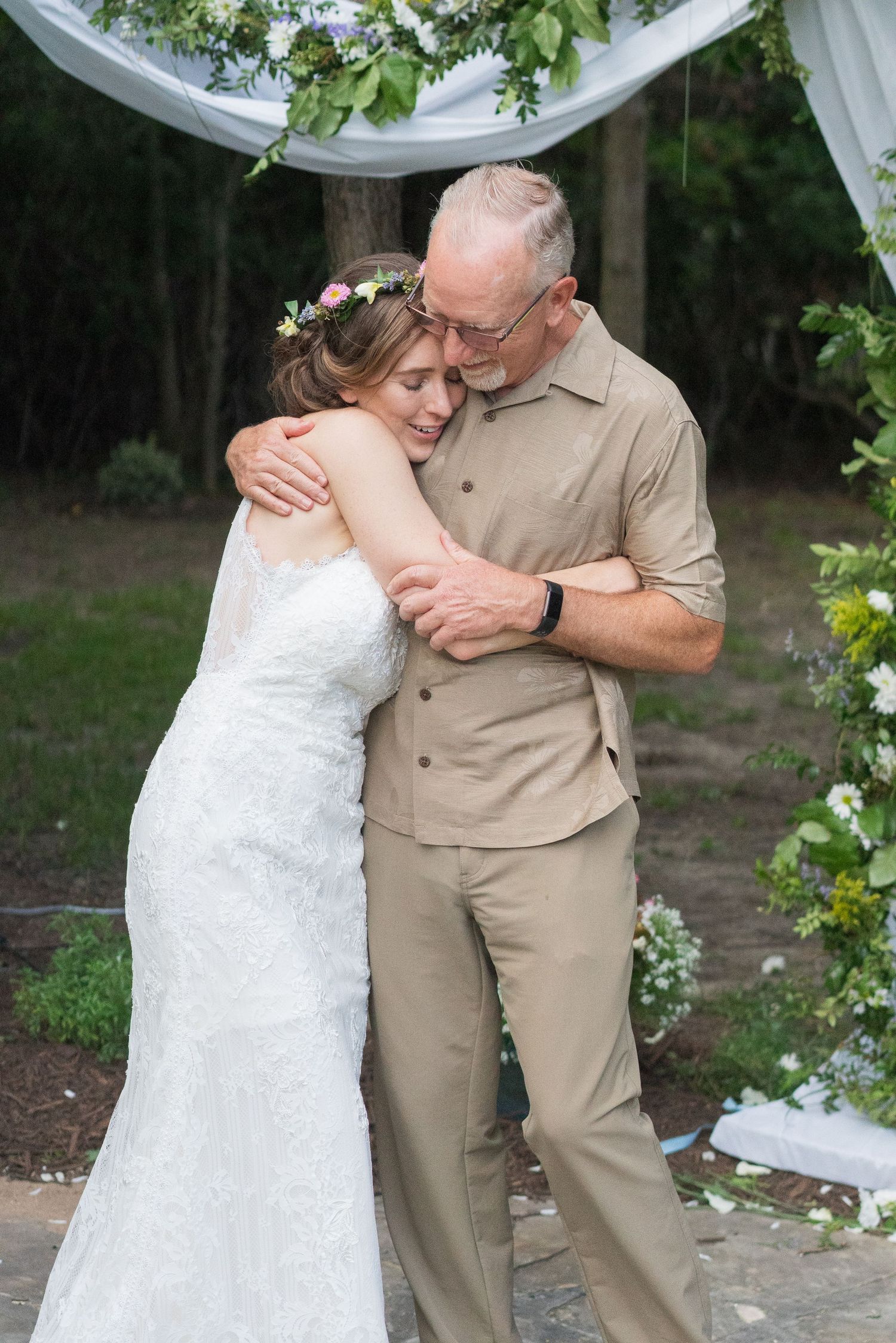 A tender dance moment captured at an outdoor wedding ceremony under white fabric draping and greenery.