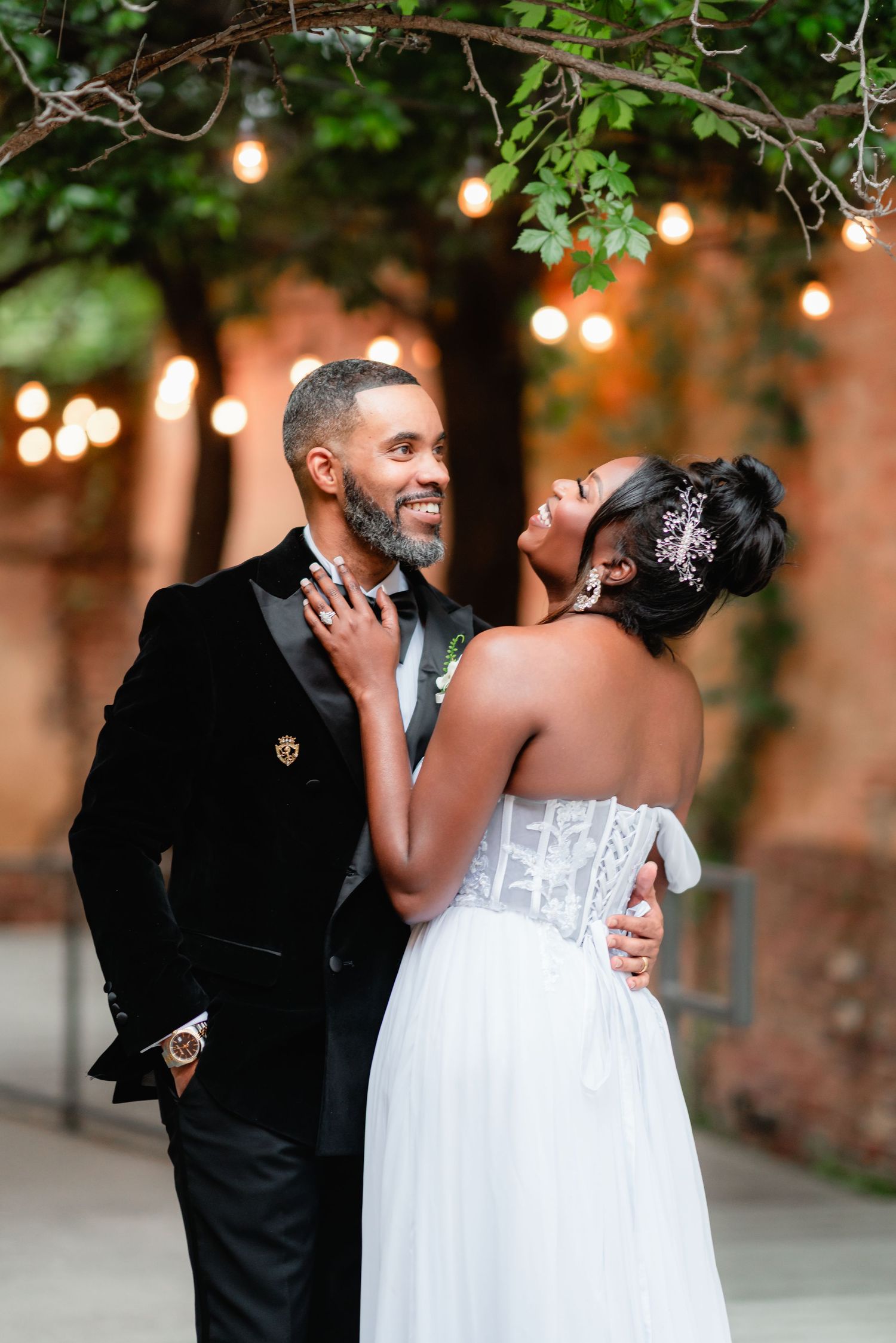 A romantic moment between newlyweds under twinkling lights at an outdoor evening wedding venue.