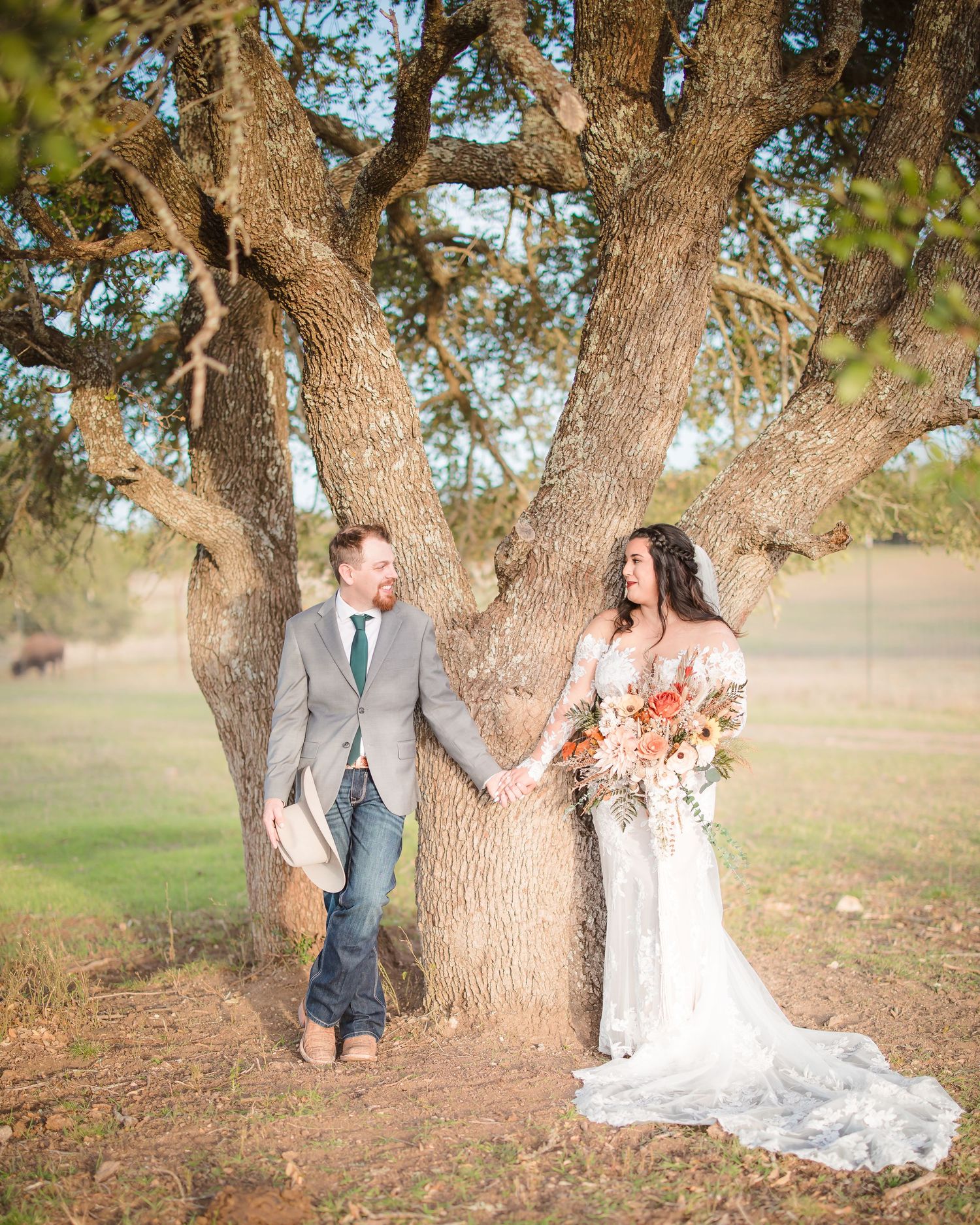A romantic wedding photo under a large oak tree with a flowing white dress and rustic charm.